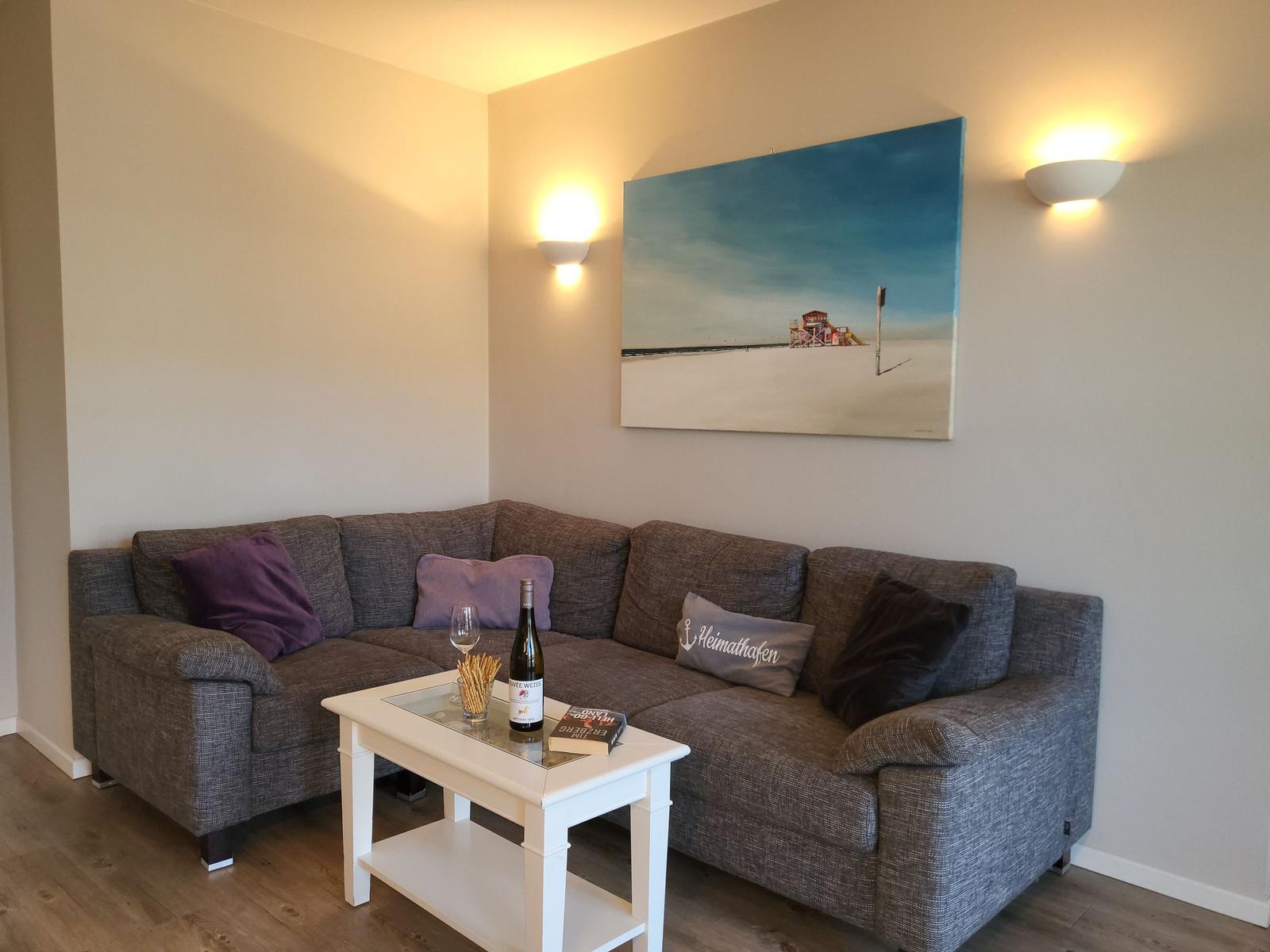 Ein Wohnzimmer mit grauem Sofa, weißem Tisch und Wandbild.