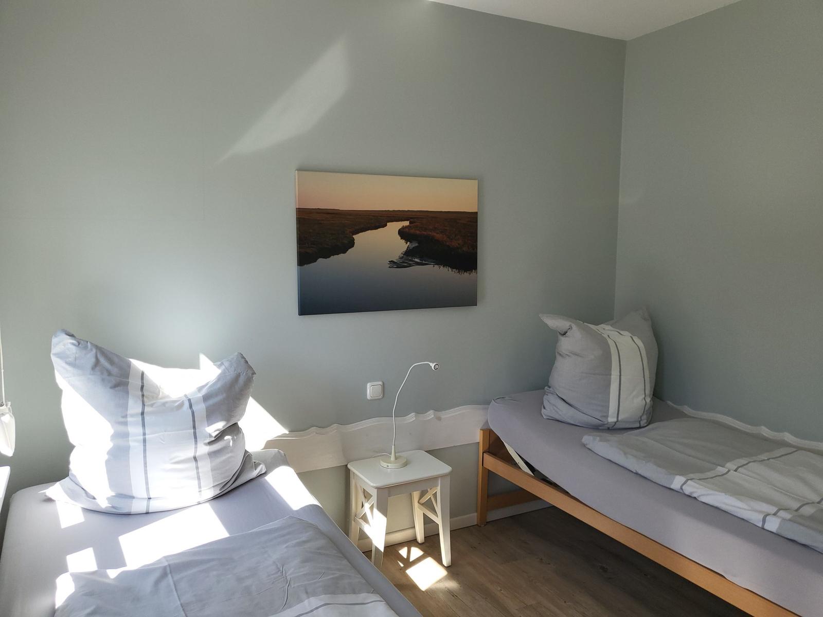 Zwei Betten mit Kissen und Decke, Wandbild und Nachttisch mit Lampe.