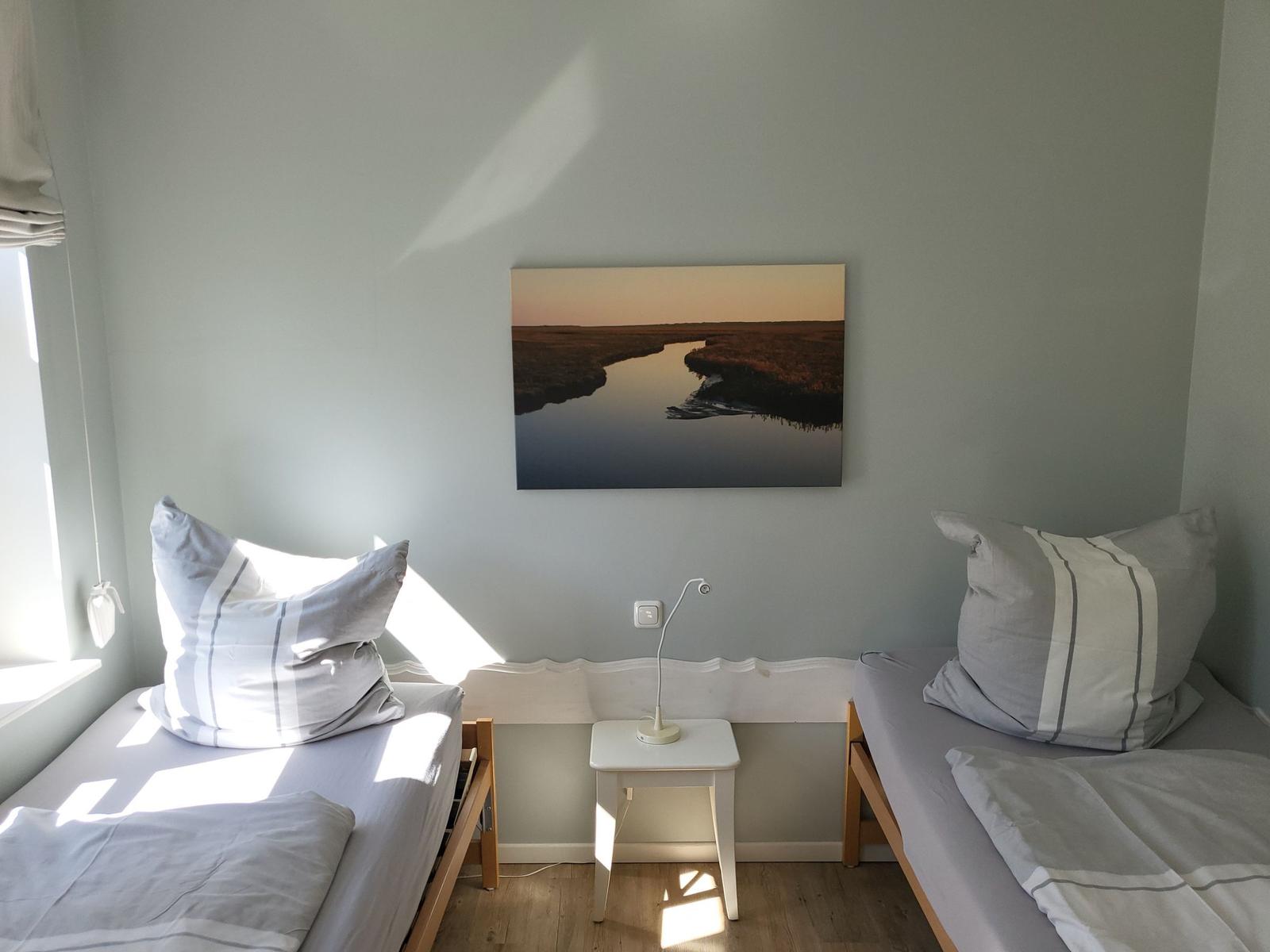 Zwei Betten mit Kissen und Bettwäsche, Wandbild und Nachttisch.