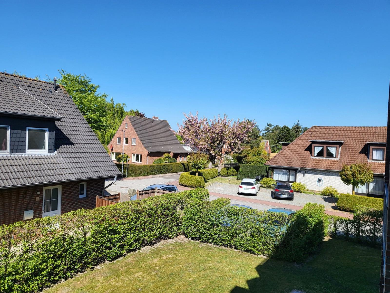 Sicht auf Wohnhäuser mit gepflegten Gärten und parkenden Autos unter blauem Himmel.