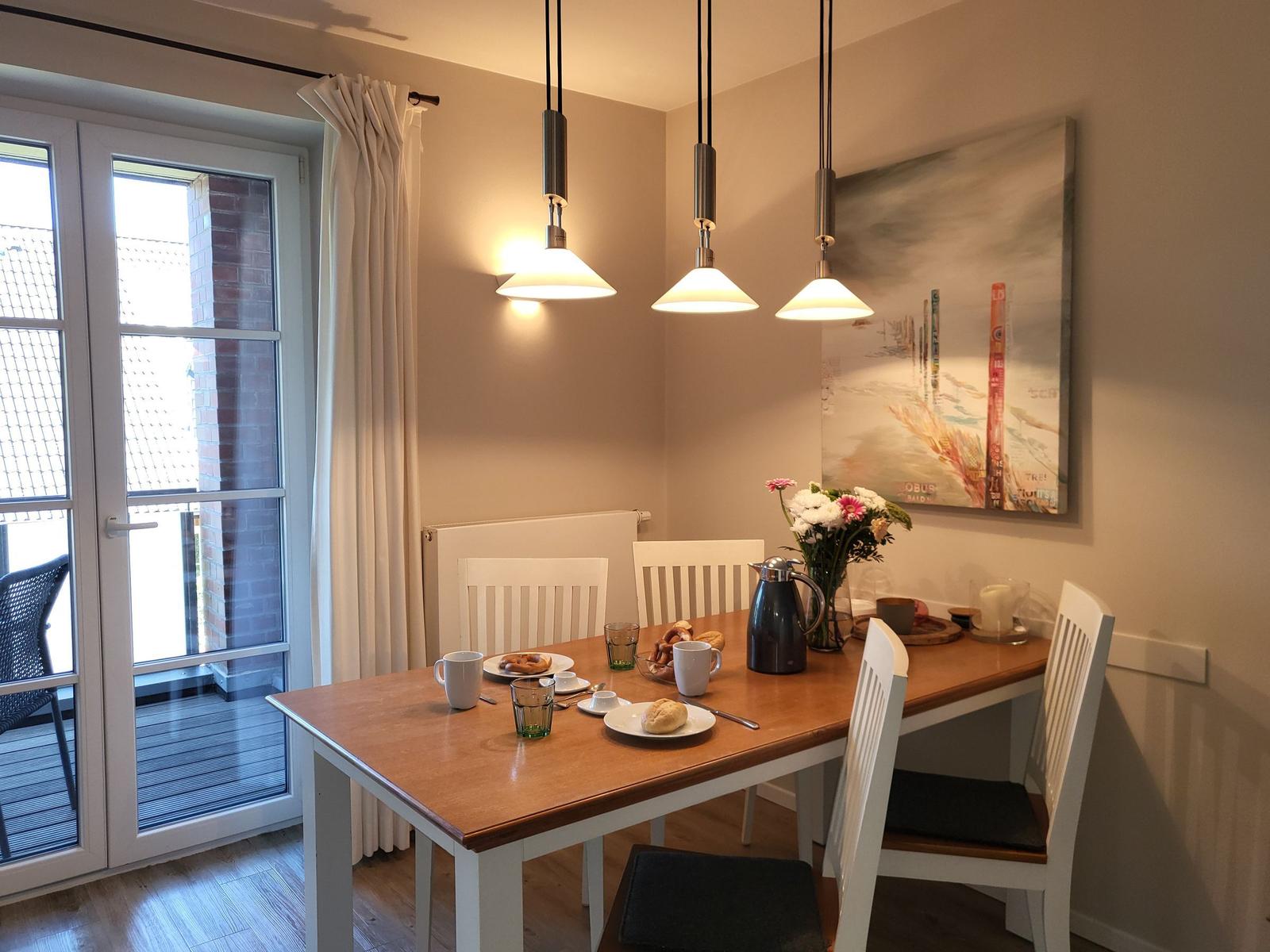 Esstisch mit vier Stühlen, drei Hängelampen und Fenster zur Terrasse.