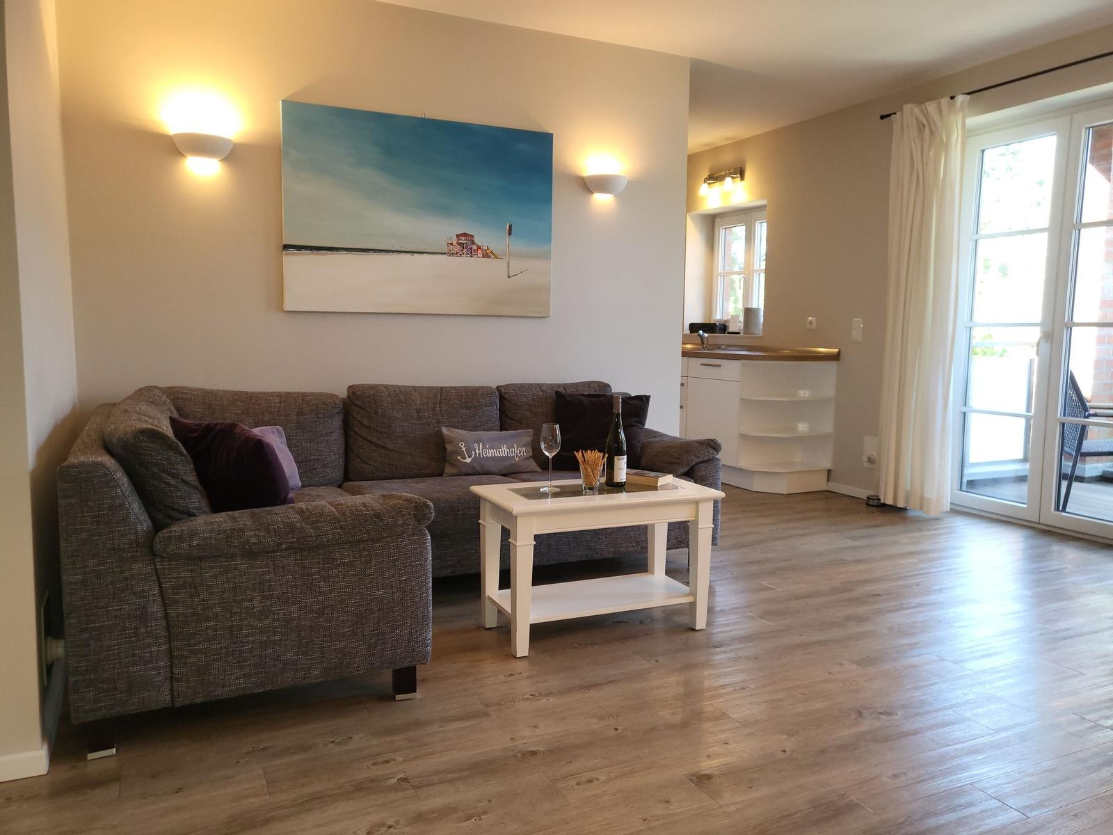 Wohnzimmer mit Sofa, Couchtisch und Wandbild. Durchgang zur Küche und Terrasse.