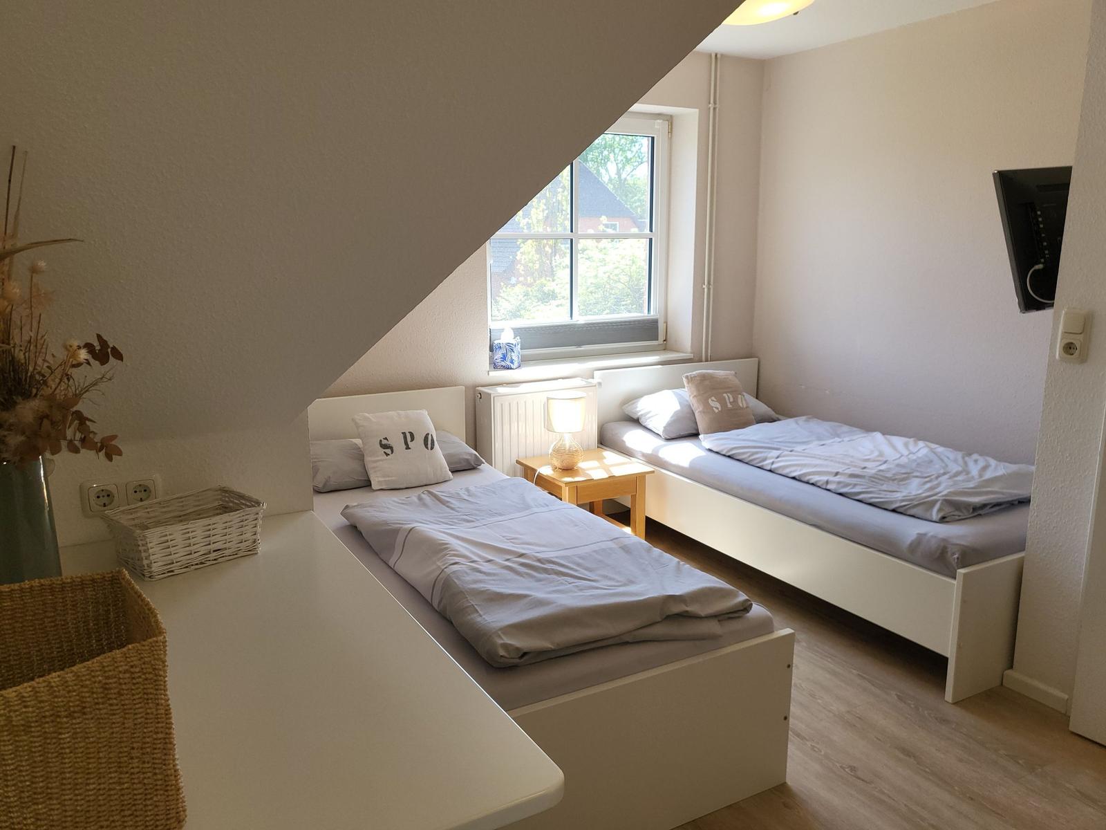 Zwei Einzelbetten unter Dachschräge mit Fenster und Nachttisch.
