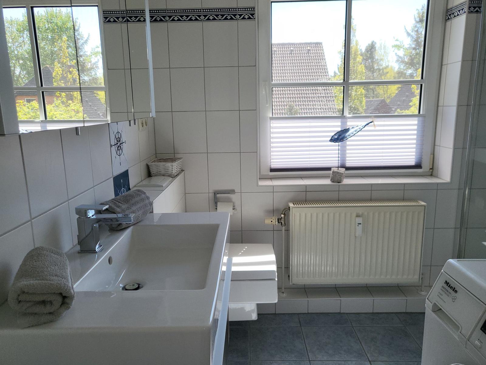 Badezimmer mit Waschbecken, Toilette, Heizkörper und Fenster mit Blick auf die Umgebung.