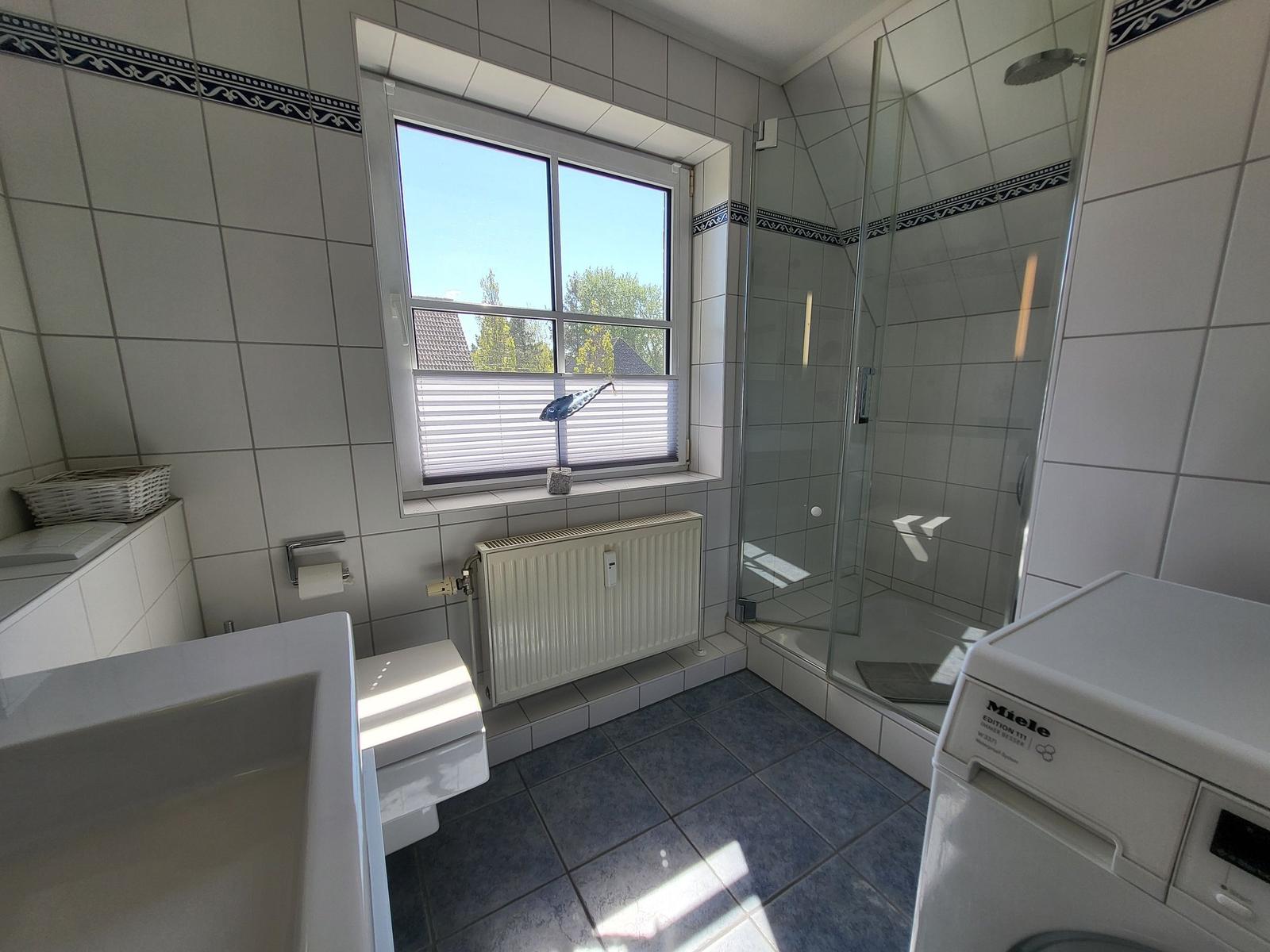 Badezimmer mit Dusche, Waschmaschine und Fenster mit Blick nach draußen.