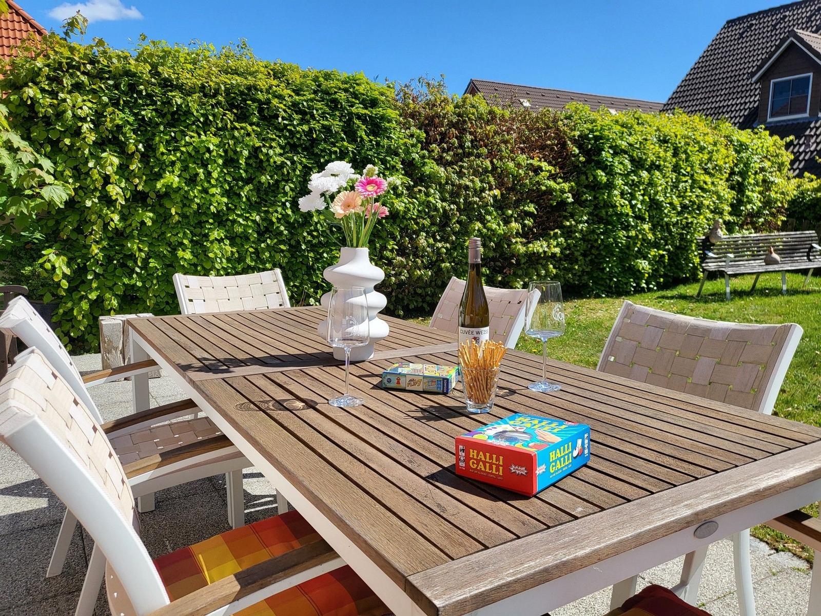Holztisch mit Stühlen, Blumen, Wein und Spielzeug im Garten.
