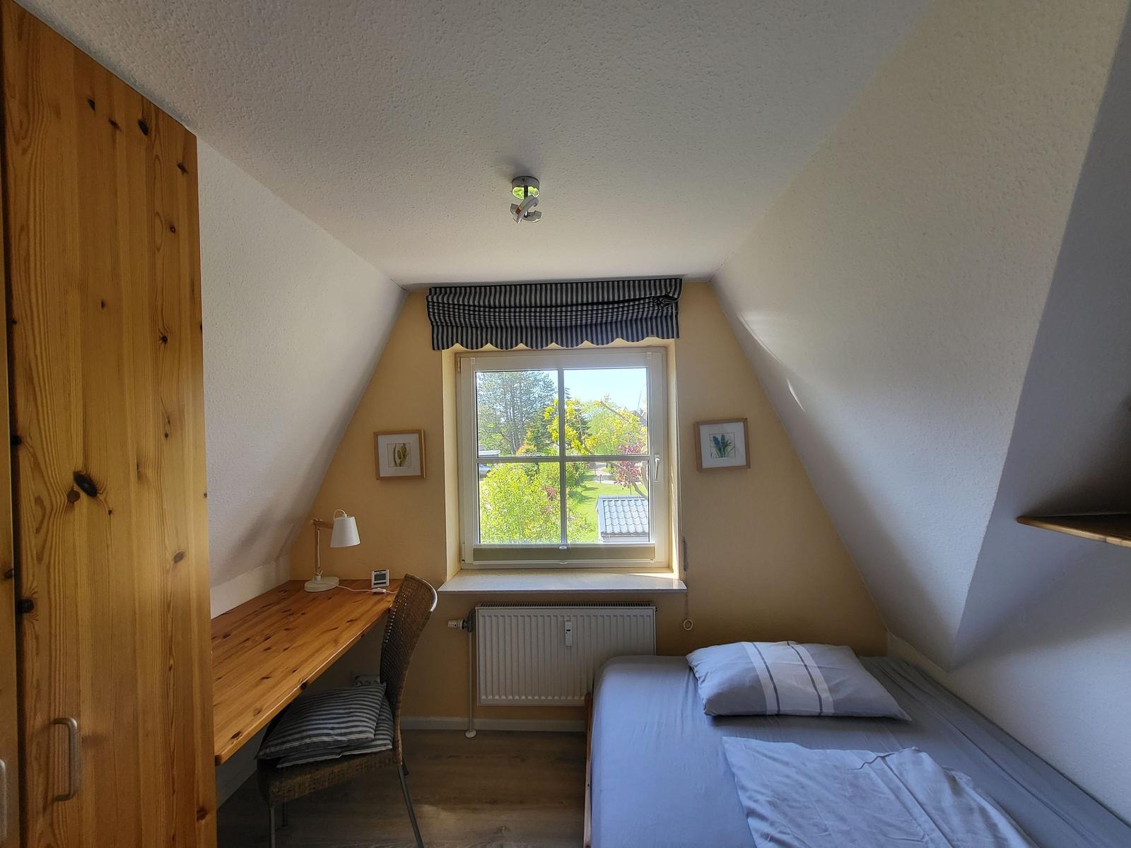 Ein Schlafzimmer mit Dachschrägen, einem Bett, Schreibtisch und Fenster mit Blick nach draußen.