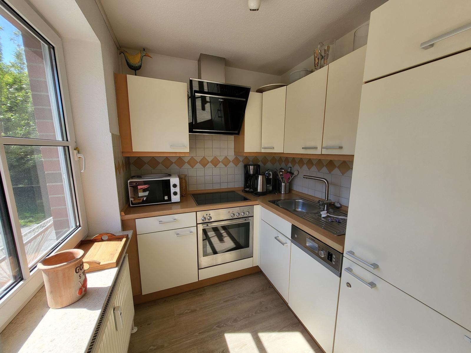 Küche mit Schränken, Herd, Spüle und Fenster. Holzfußboden und Backofen.
