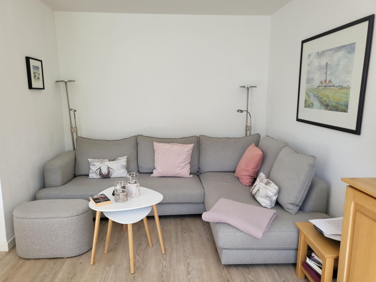 Ein Wohnzimmer mit grauem Ecksofa, runden Tisch und Wandbild.