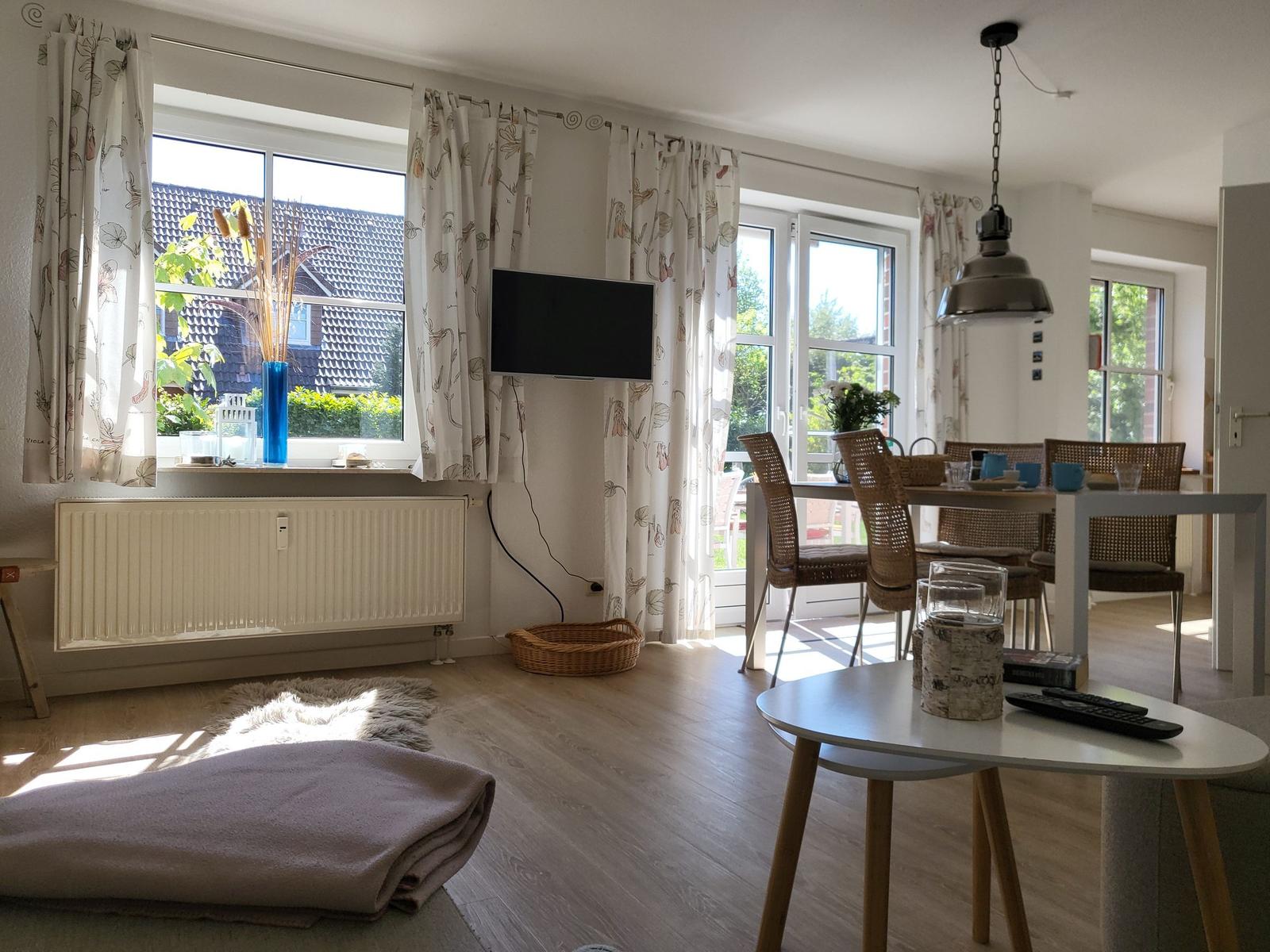 Wohn- und Essbereich mit TV, Tisch und Stühlen, Fenstern und Vorhängen.