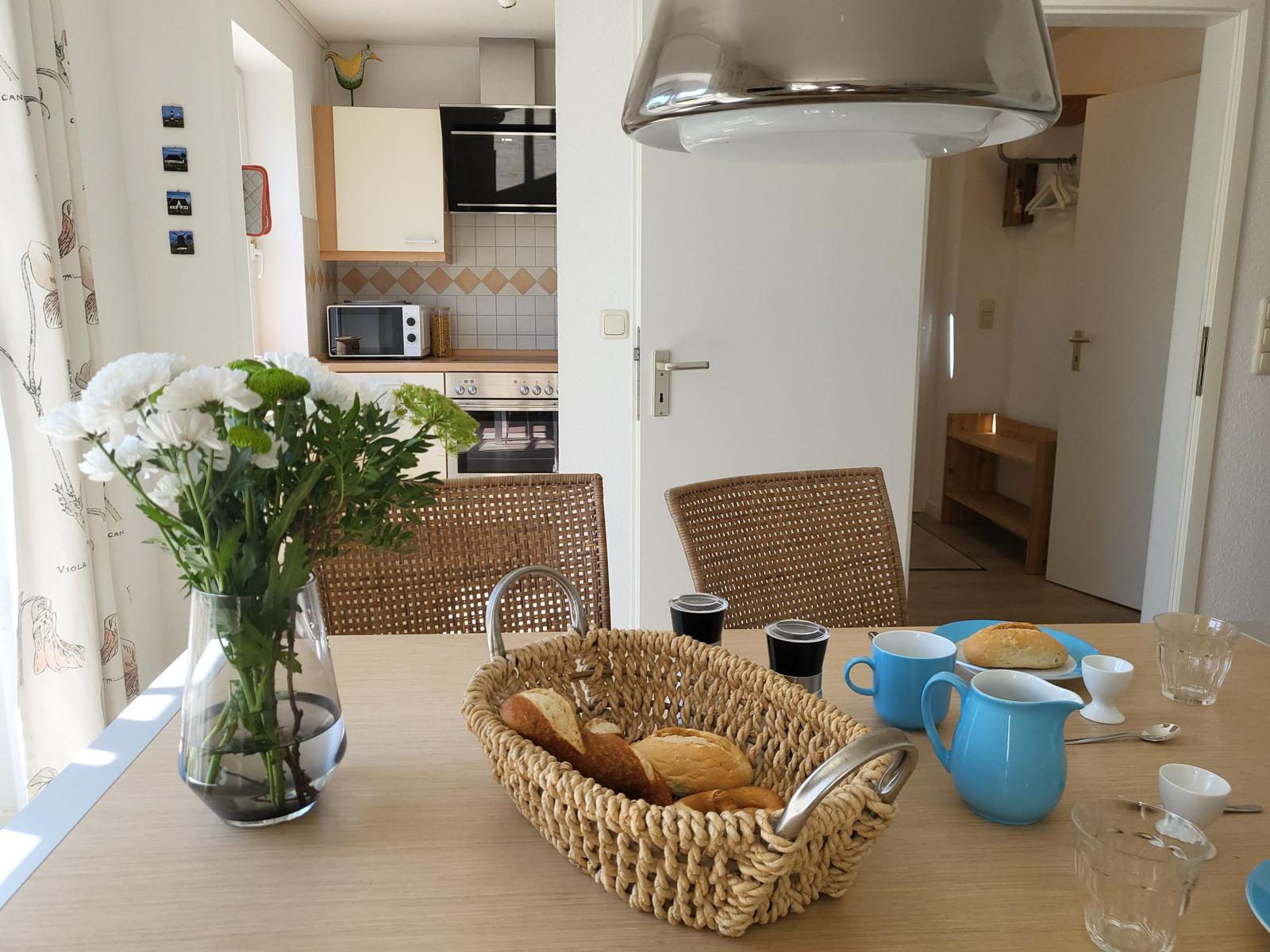 Esstisch mit Korb voller Brot, Blumen und blauen Tassen.