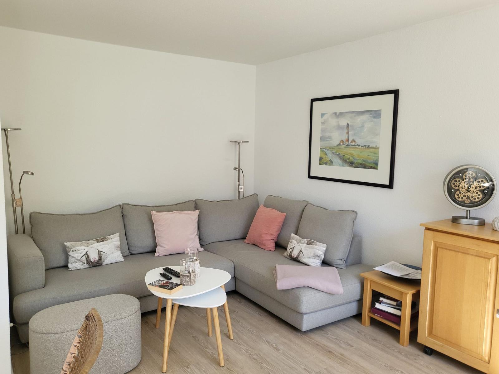 Ein Wohnzimmer mit grauem Sofa, dekorativen Kissen und einem runden Tisch.