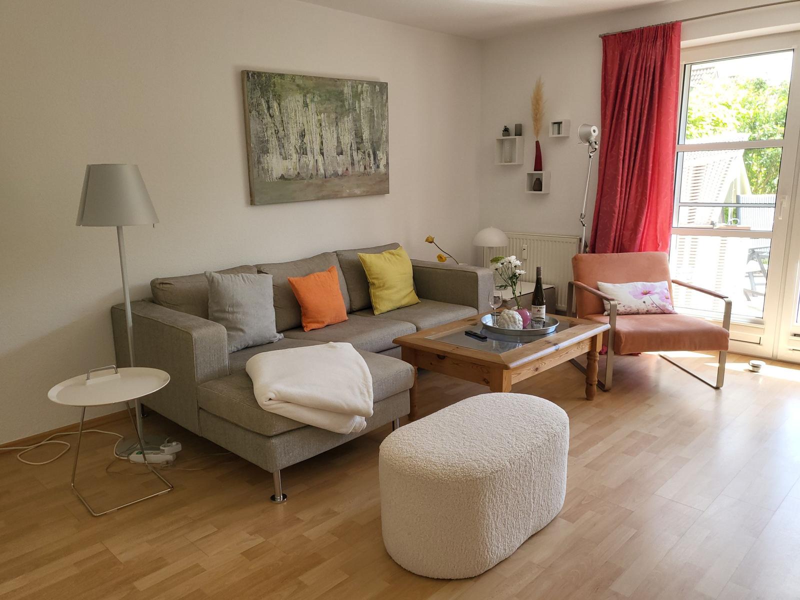 Wohnzimmer mit Sofa, Sessel und Couchtisch. Rote Vorhänge vor Fenster.