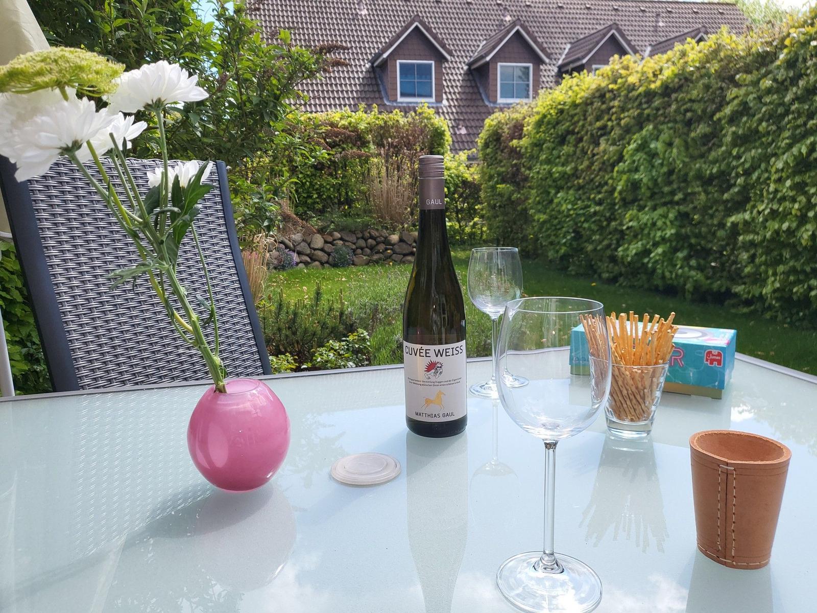 Garten-Tisch mit Wein, Gläsern, Crackern und Blumen. Hintergrund: Haus und Grünflächen.