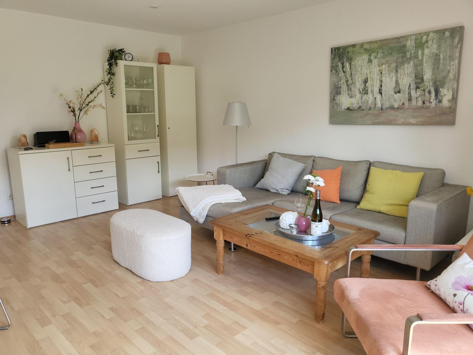 Wohnzimmer mit Sofa, Couchtisch und Holzboden. An der Wand hängt ein großes Bild.