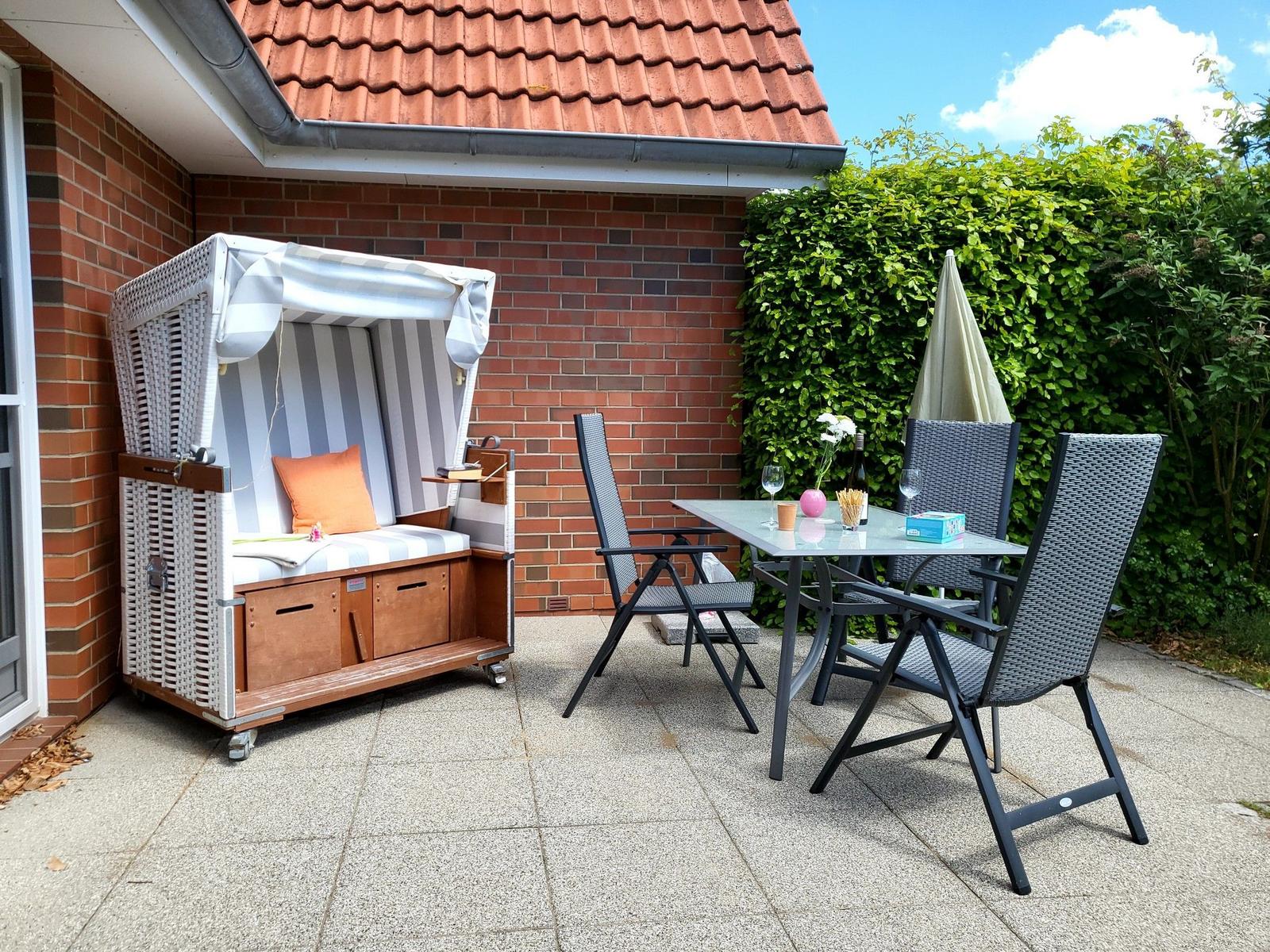 Terrasse mit Strandkorb, Tisch und Stühlen vor Backsteinmauer