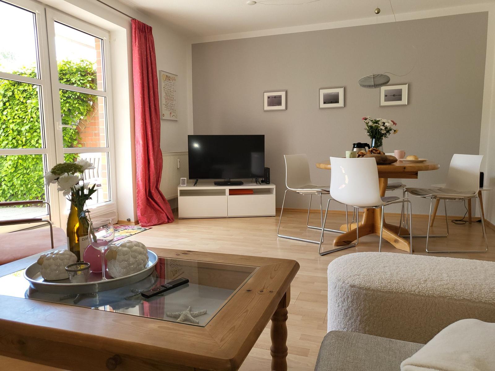 Wohn- und Essbereich mit Fernseher, Esstisch und Fenster zur Außenterrasse.