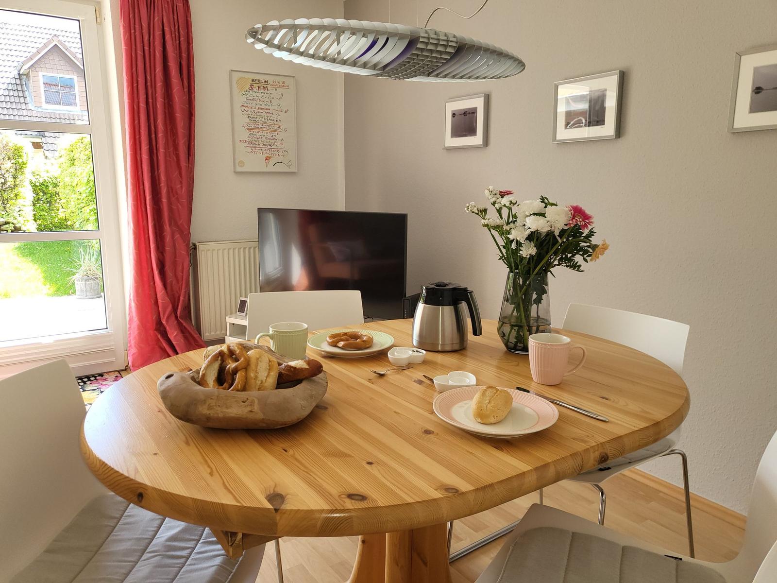 Rundes Holztablett mit Frühstück, Blumen und Kaffeemaschine.
