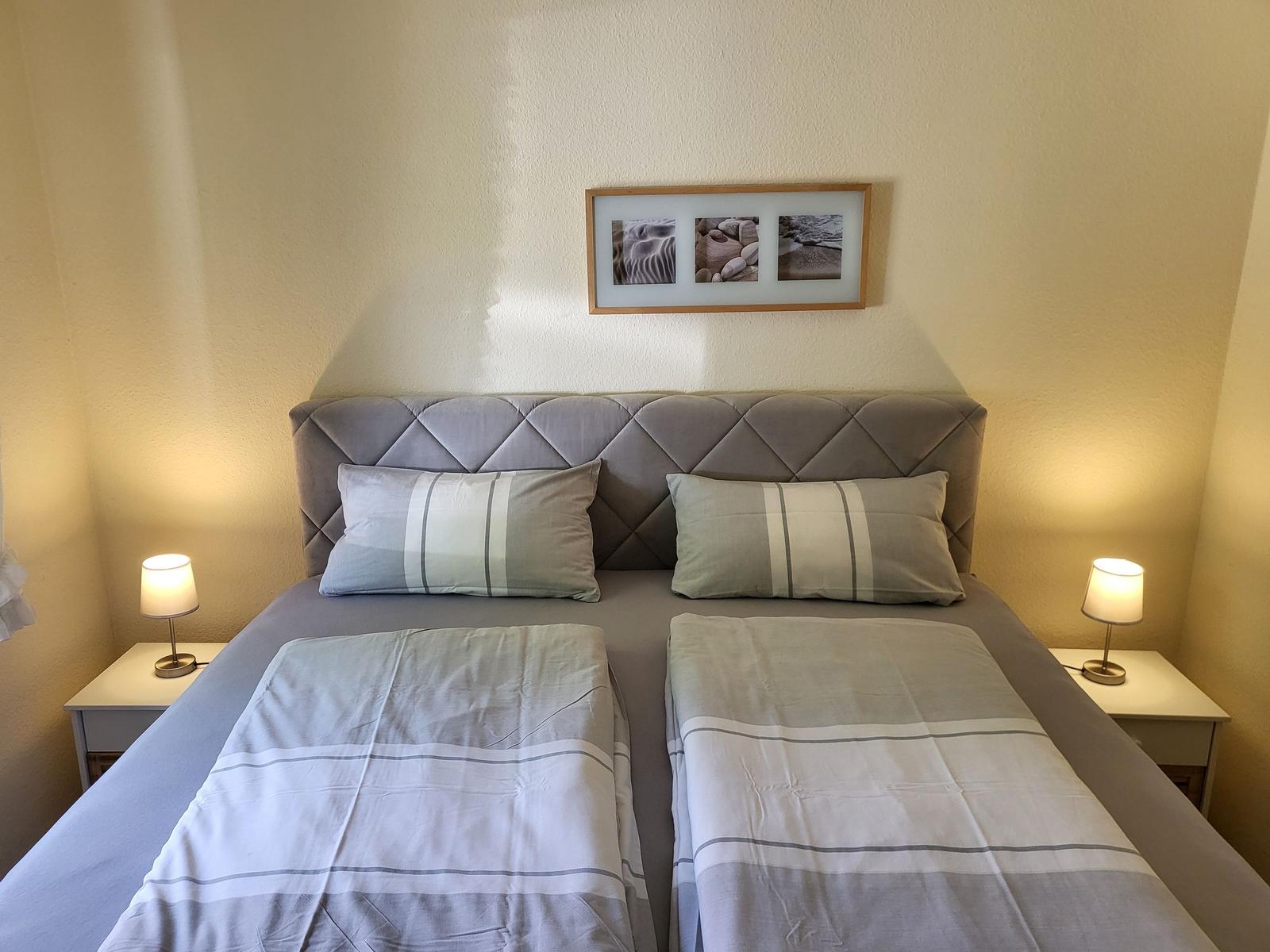 Schlafzimmer mit Doppelbett, Kopfteil, zwei Nachttischen und Lampen.