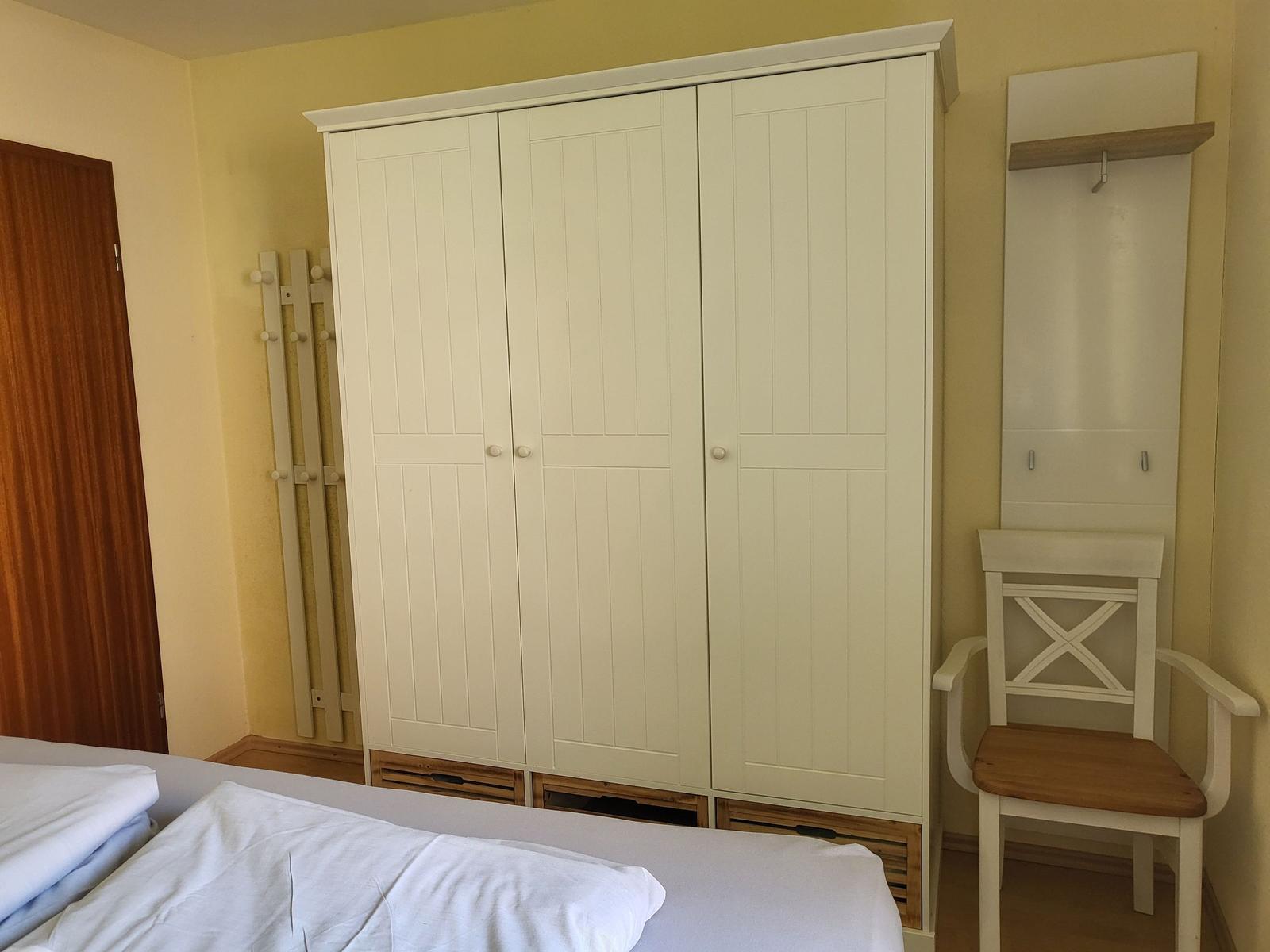 Schlafzimmer mit weißem Kleiderschrank, Stuhl und Heizkörper an der Wand.