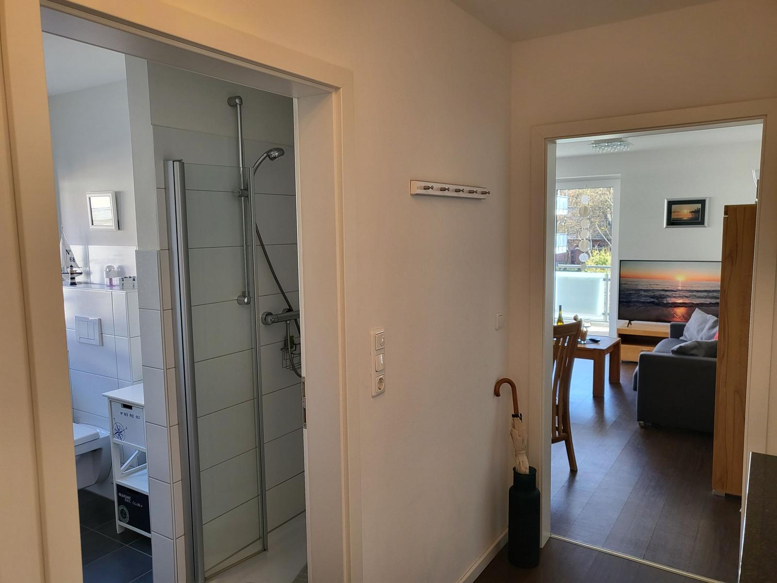 Badezimmer mit Dusche und Toilette. Wohnzimmer mit Sofa und Fernseher.