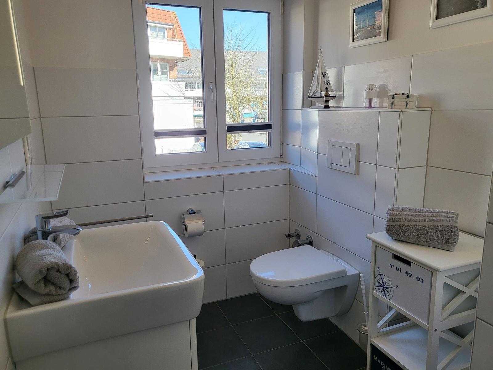 Badezimmer mit Waschbecken, WC und Fenster. Dekoration mit Segelboot und Handtuch.