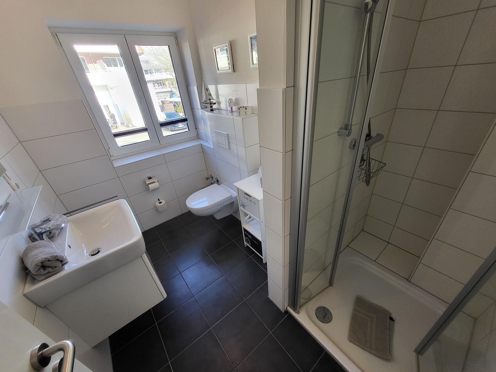 Badezimmer mit Dusche, Toilette und Waschbecken. Fenster mit Blick nach außen.