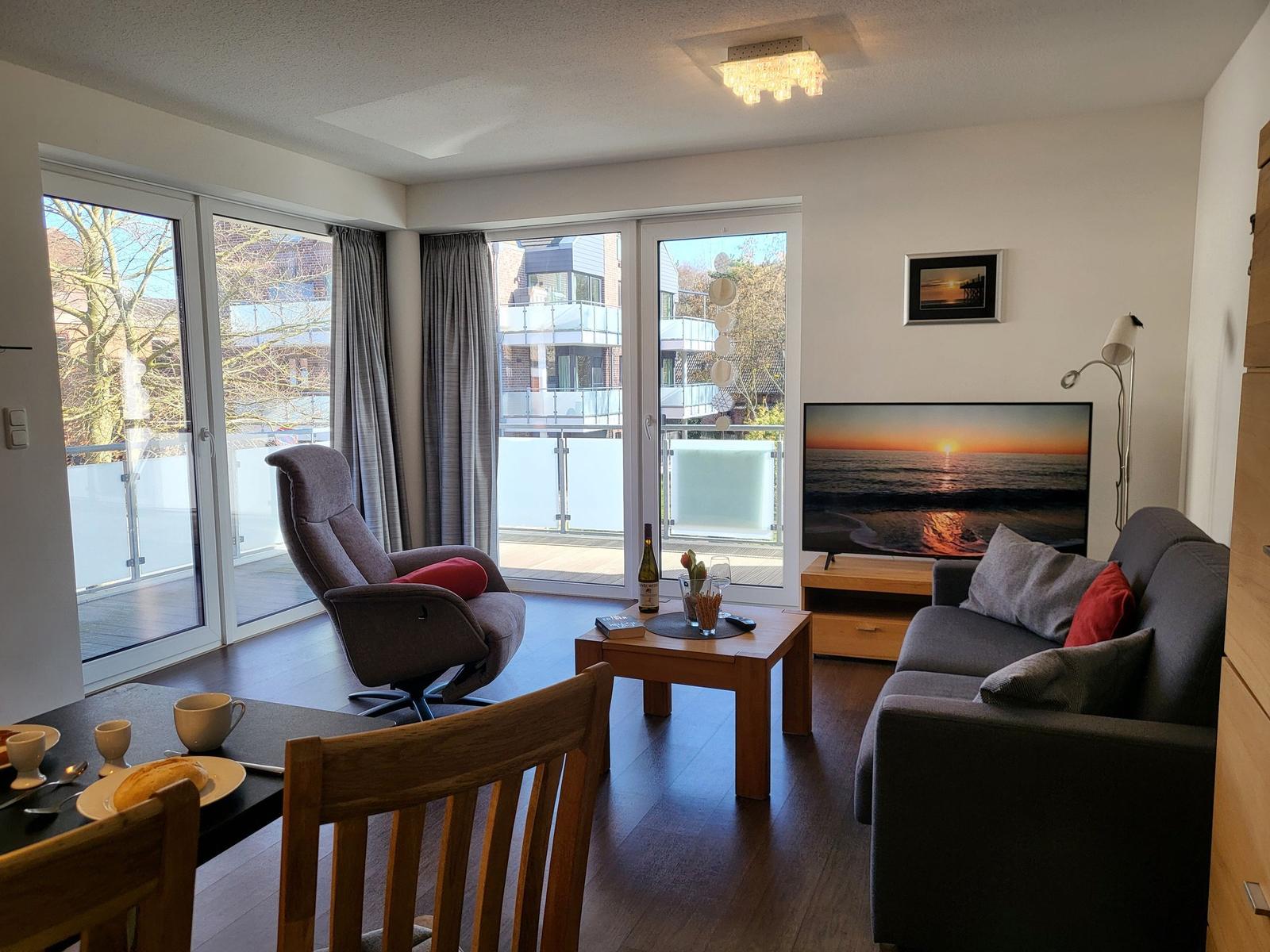 Wohn- und Essbereich mit Sofa, Sessel, TV und Balkonansicht.