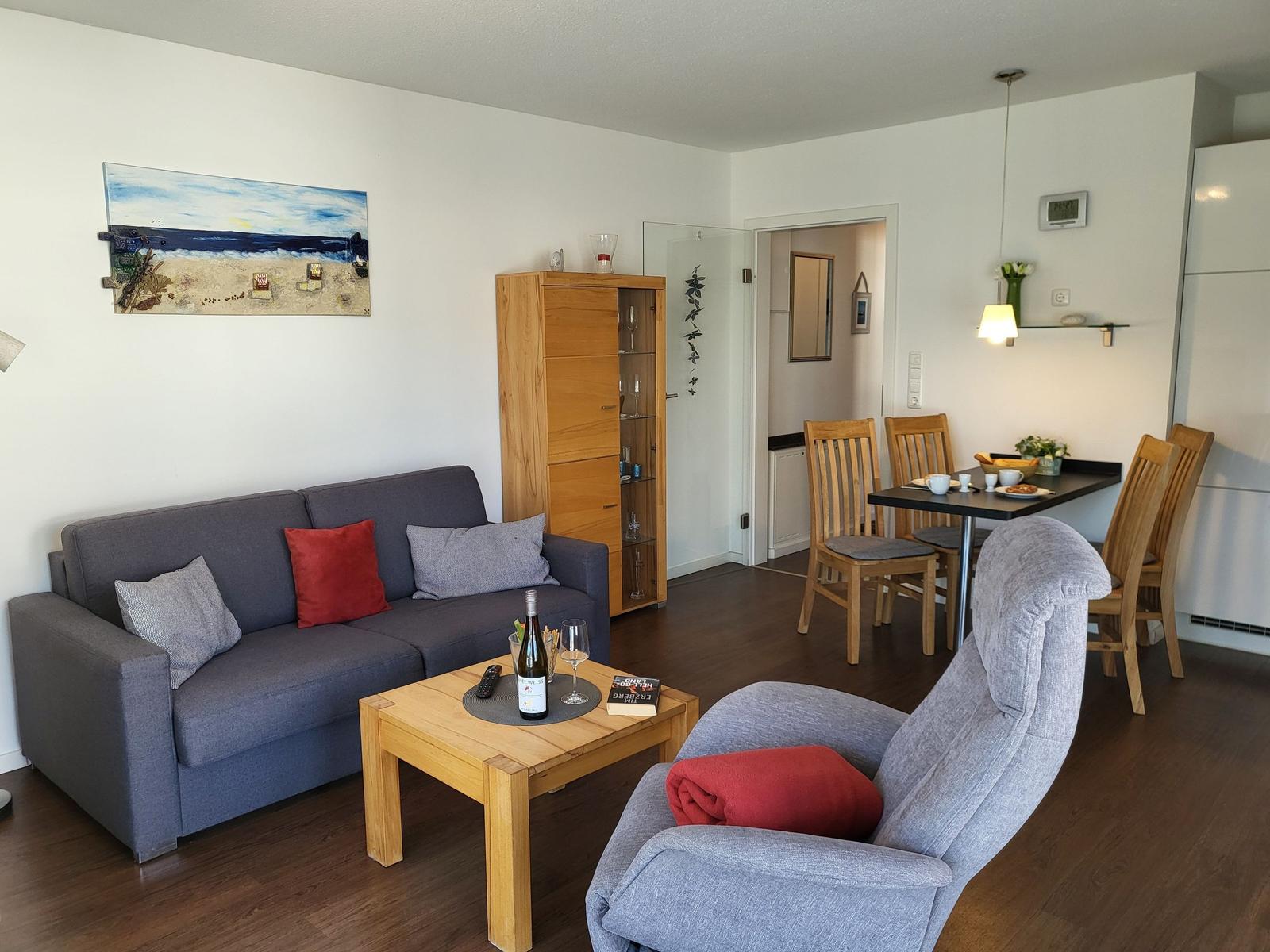 Wohn- und Essbereich mit Sofa, Sessel, Tisch und Stühlen. Wandbild und Holzmöbel.