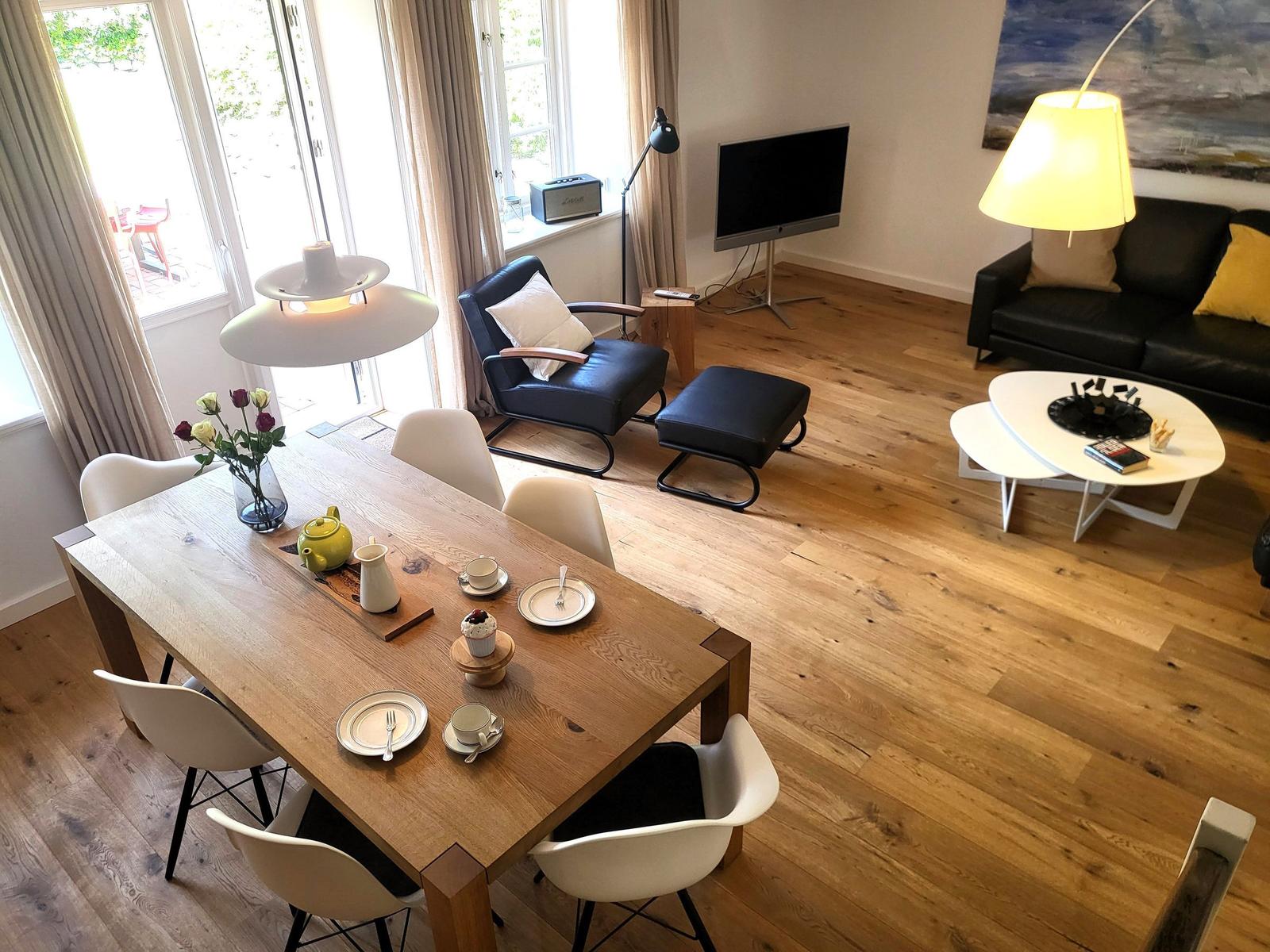 Essbereich mit Holztisch und Stühlen. Wohnbereich mit Sofa, Couchtisch und Fernseher.