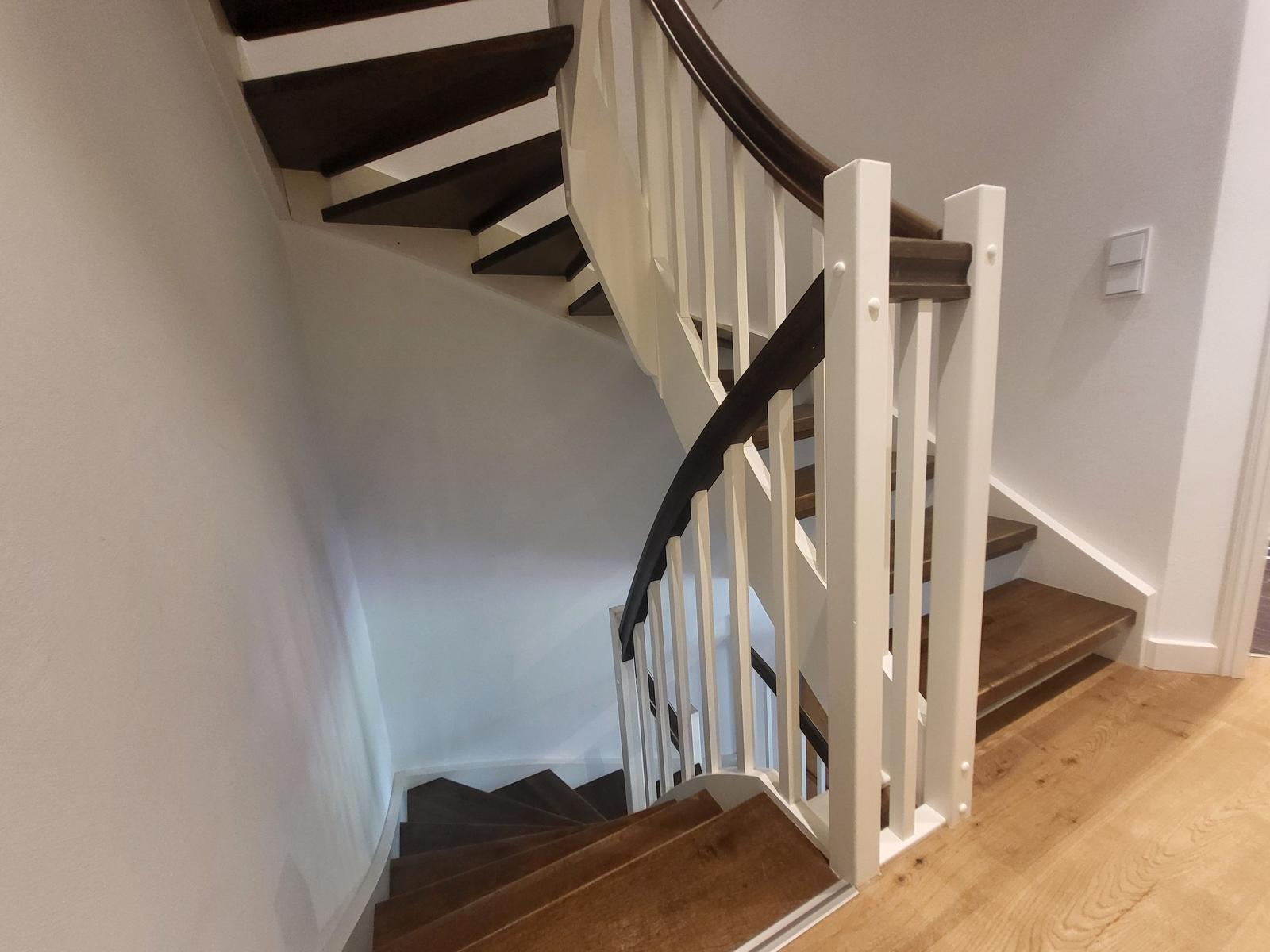 Eine Treppe mit dunklen Stufen und weißer Balustrade führt nach oben.