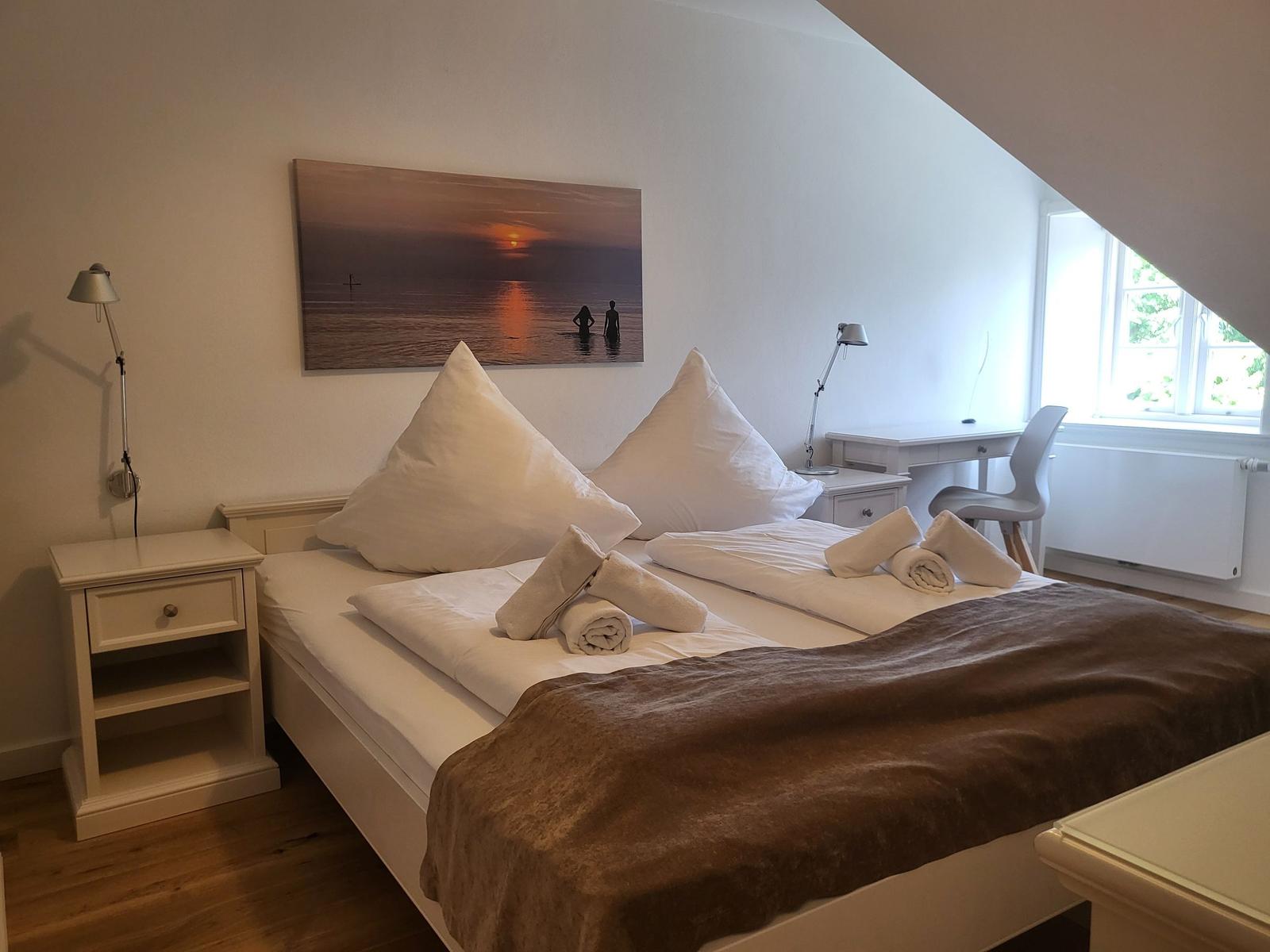 Schlafzimmer mit Bett, Nachttisch, Schreibtisch und Fenster.