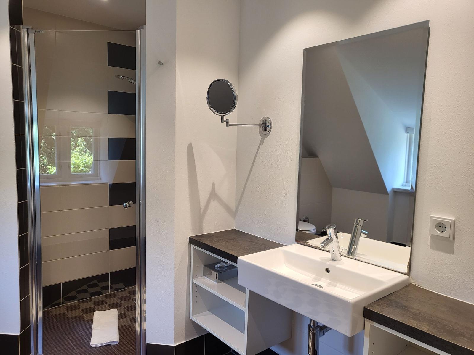 Badezimmer mit Dusche, Waschbecken und Spiegel. Duschbereich mit Fenster.