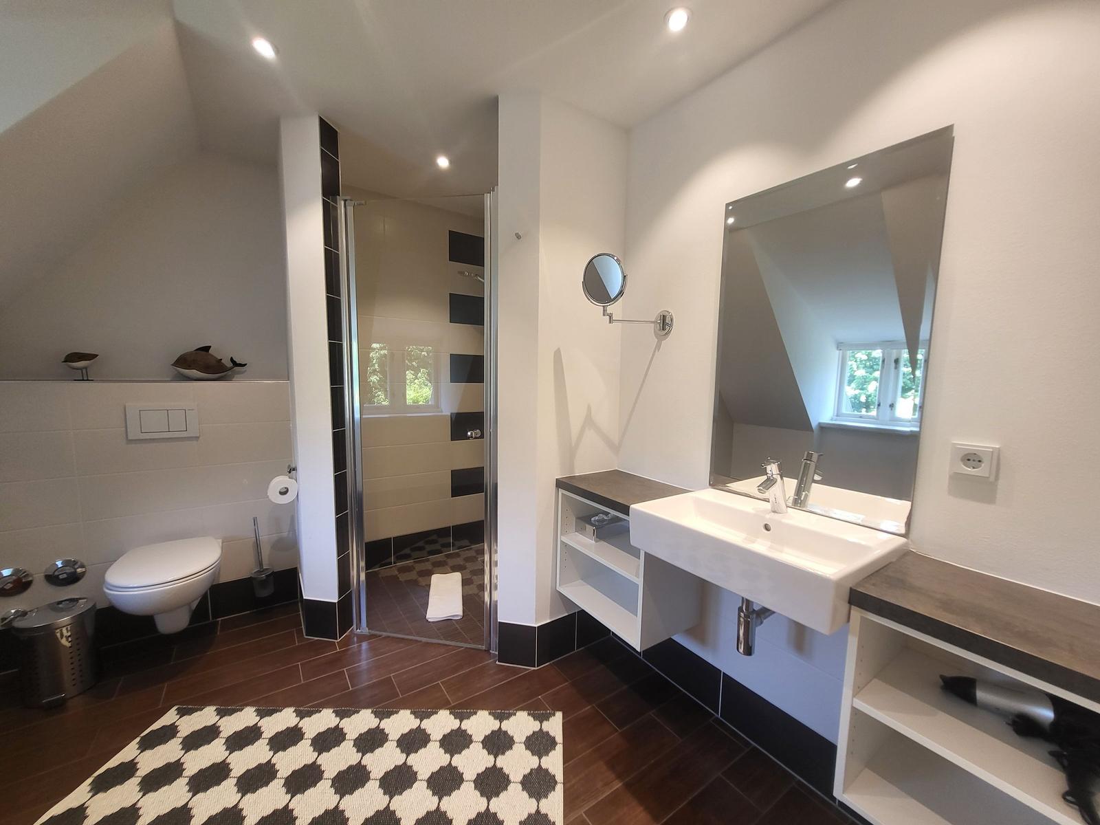 Badezimmer mit Dusche, Waschbecken und Toilette. Schwarze und weiße Fliesen.