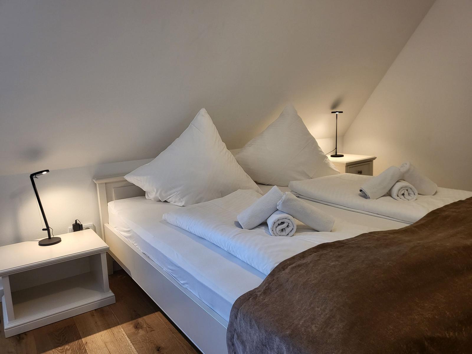 Schlafzimmer mit Doppelbett, zwei Nachttischen und einer braunen Bettdecke.