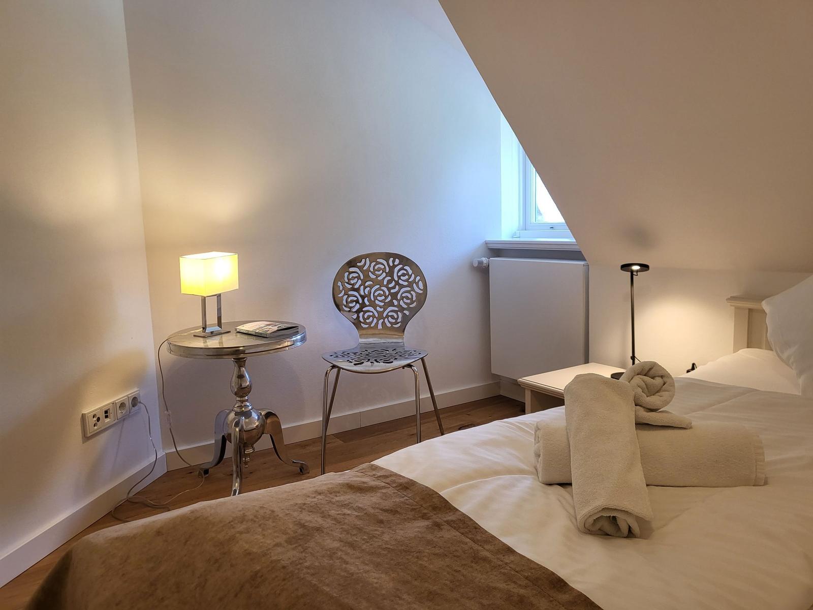 Schlafzimmer mit Bett, Stuhl und Tisch unter schrägem Dach