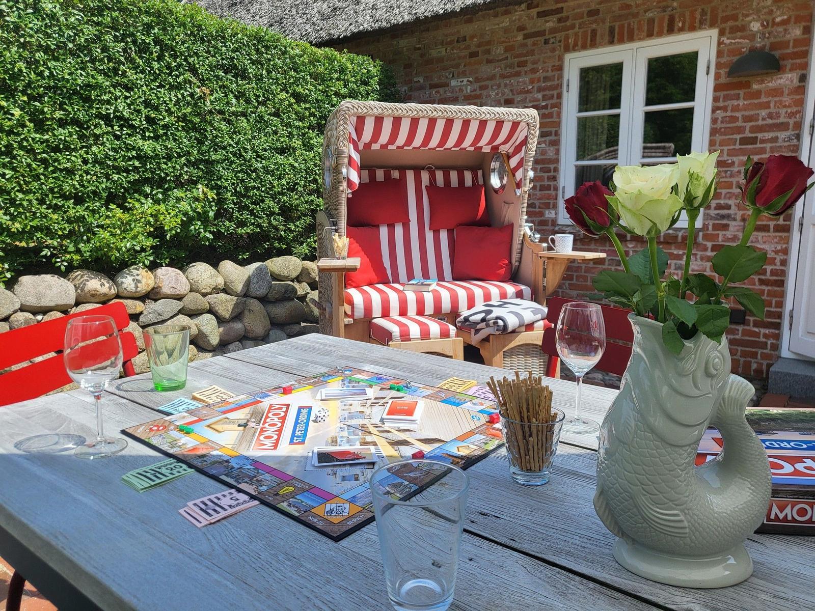 Außenbereich mit Strandkorb, Tisch und Blumen. Spiel und Getränke auf dem Tisch.