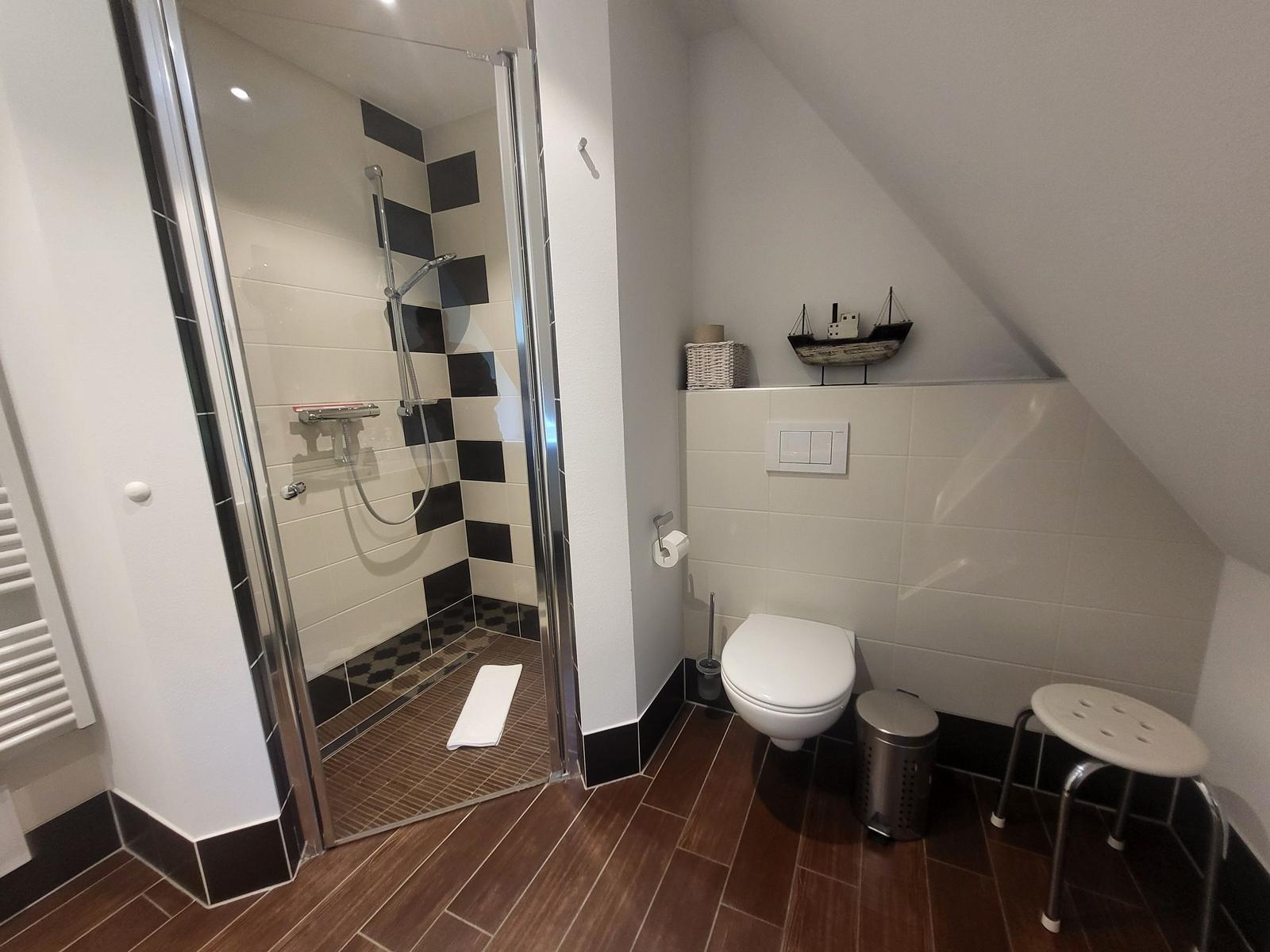 Bad mit Dusche, Toilette und Sitzhocker unter Dachschrägen.