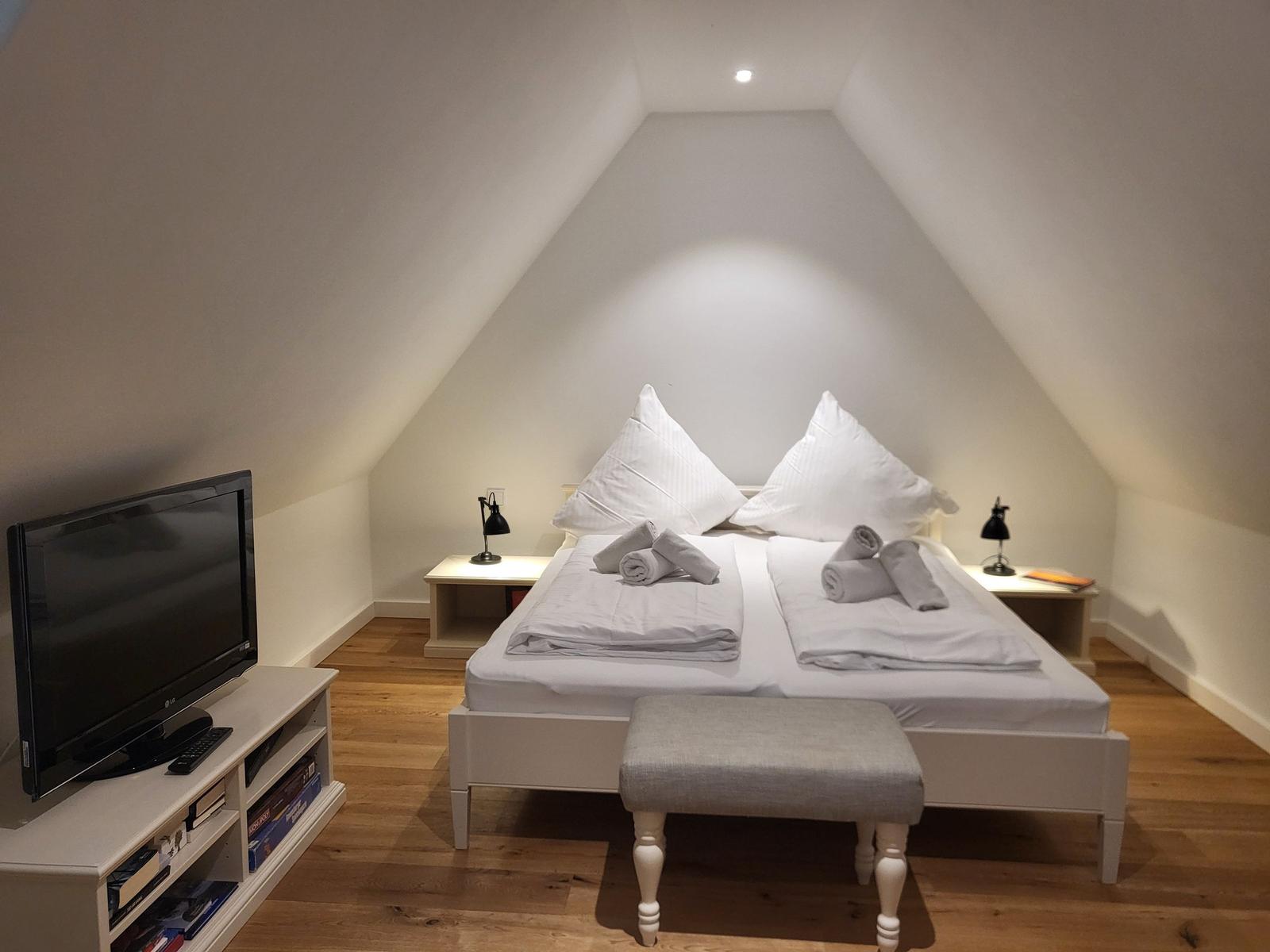 Schlafzimmer mit Dachschrägen, Bett, Nachttische und Fernseher.