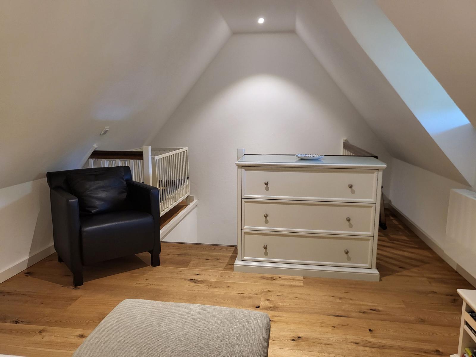 Schlafzimmer mit Dachschrägen, schwarzer Ledercouch, weißem Schrank und Holzboden.