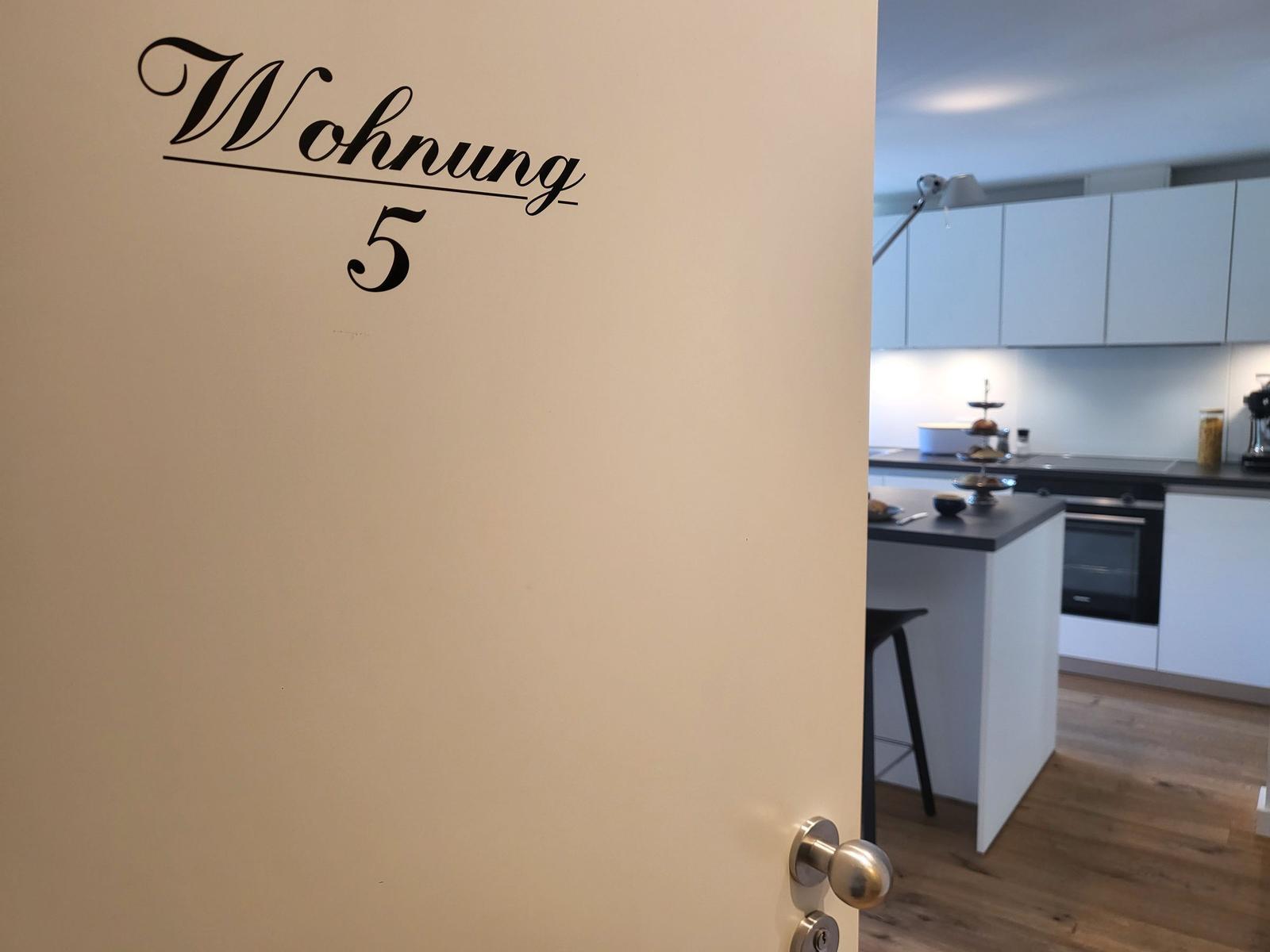 Tür mit Aufschrift Wohnung 5 öffnet zu einer Küche mit Arbeitsplatte und Schränken.