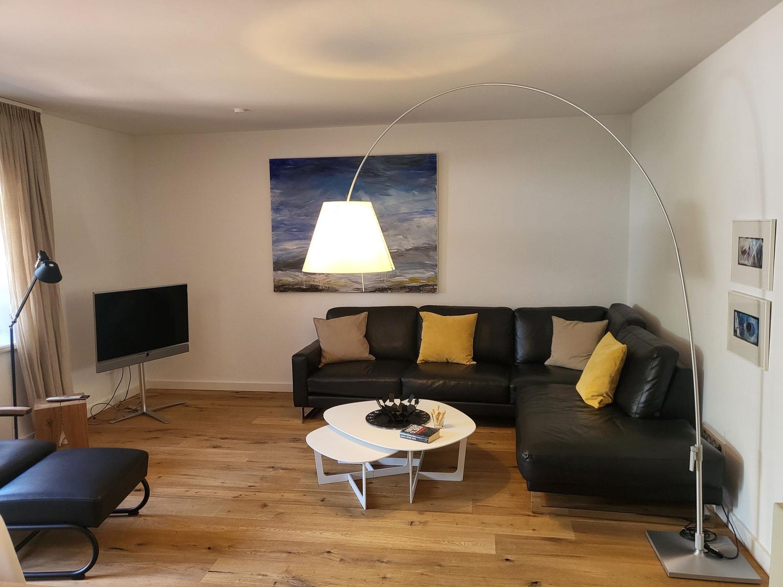 Wohnzimmer mit schwarzer Couch, weißem Couchtisch und Bodenheizung.