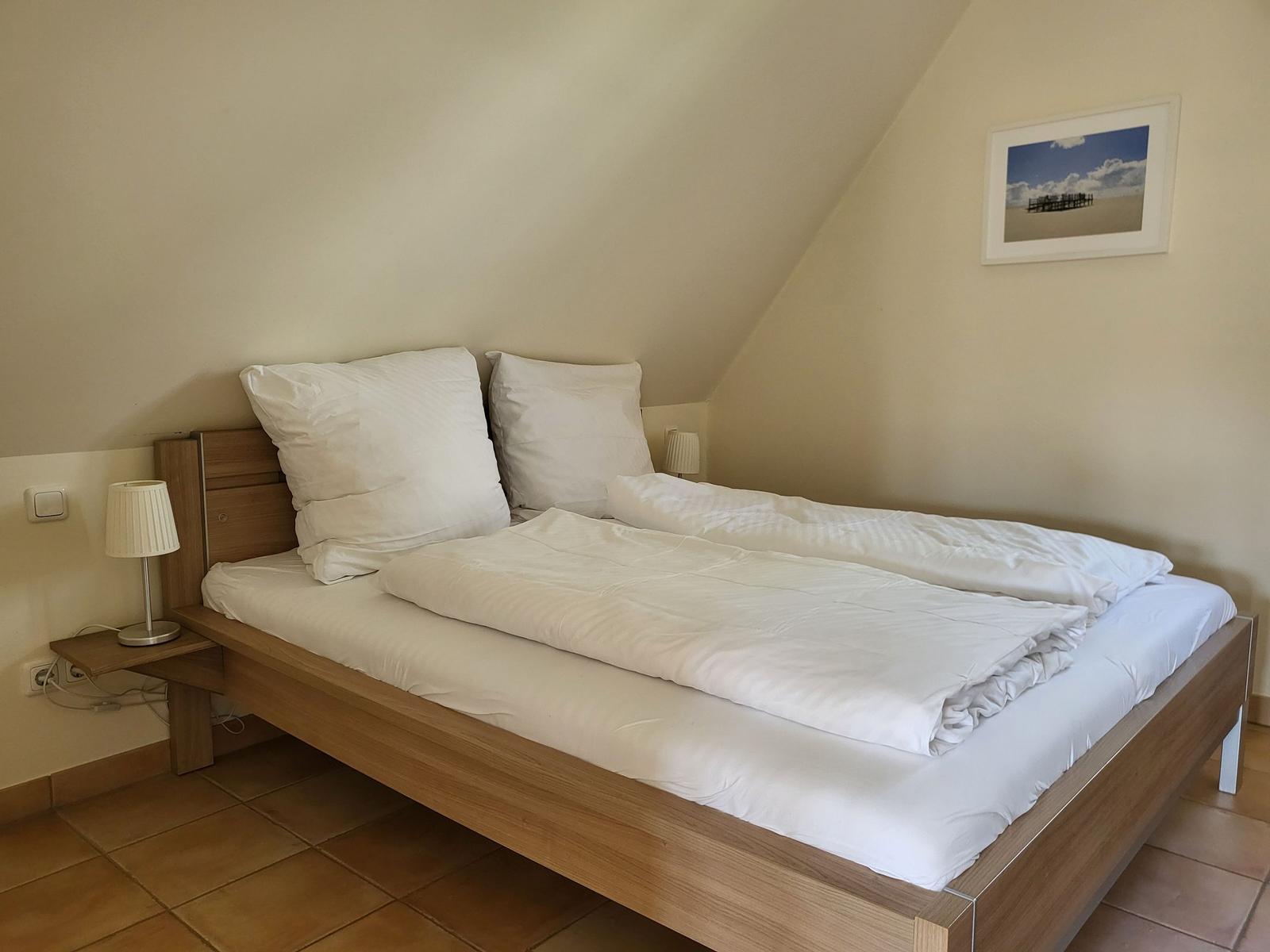 Schlafzimmer mit Doppelbett, Holzgestell und Stehleuchte an der Wand