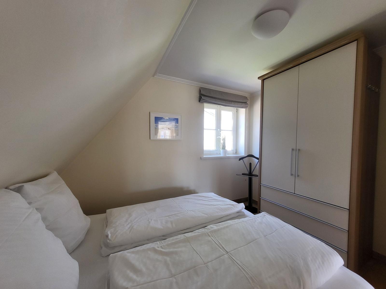 Schlafzimmer mit Dachschrägen, Bett, Kleiderschrank und Fenster mit Pflanze.