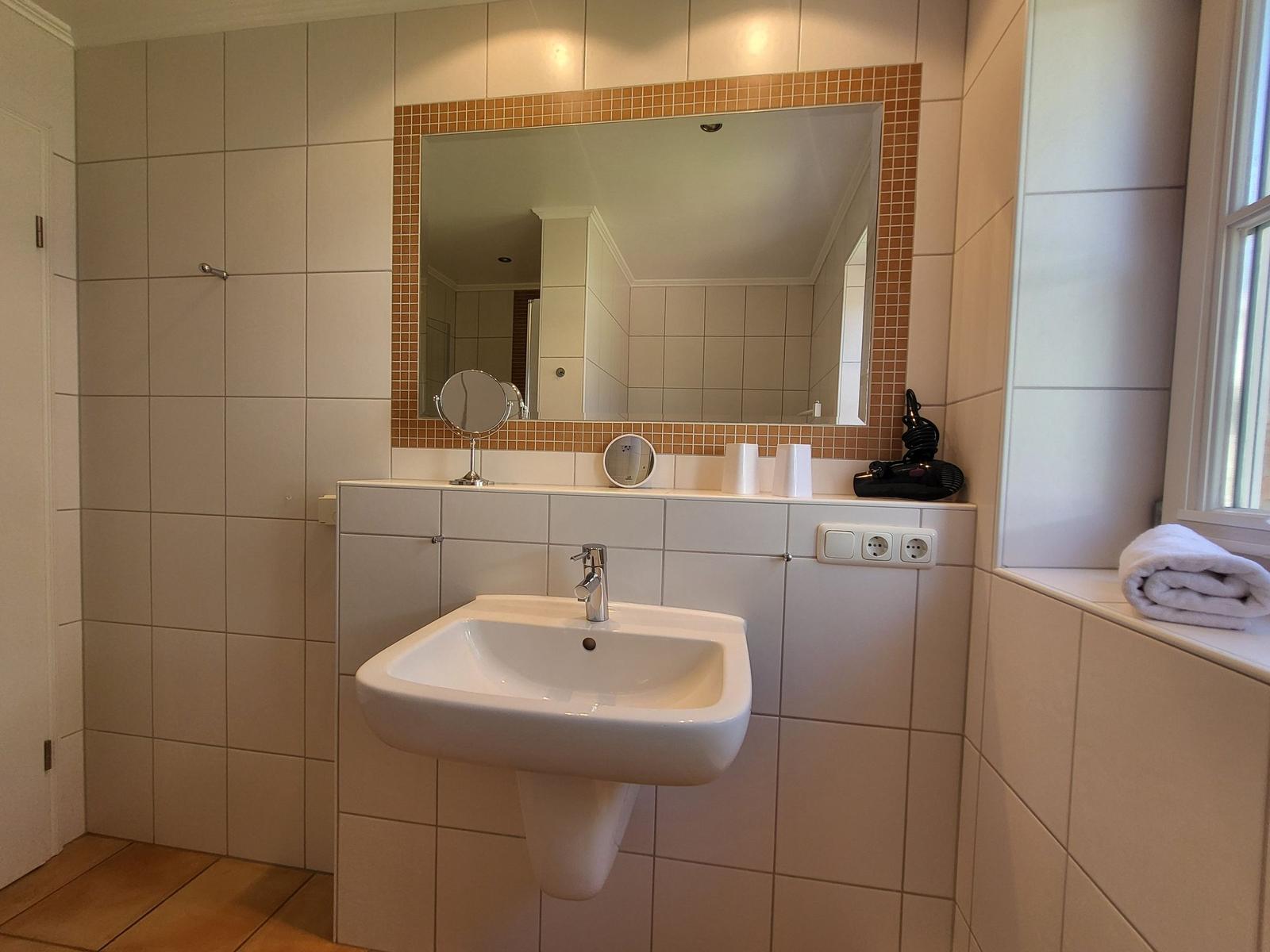 Badezimmer mit Waschbecken, Spiegel und Fenster. Handtuch und Haartrockner sind vorhanden.
