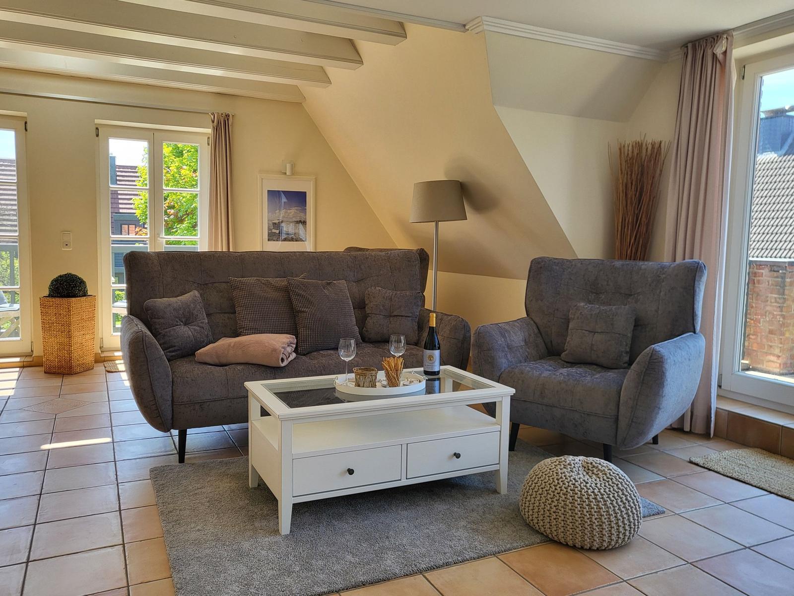 Wohnzimmer mit Sofa, Sessel, Couchtisch und Fenstern.