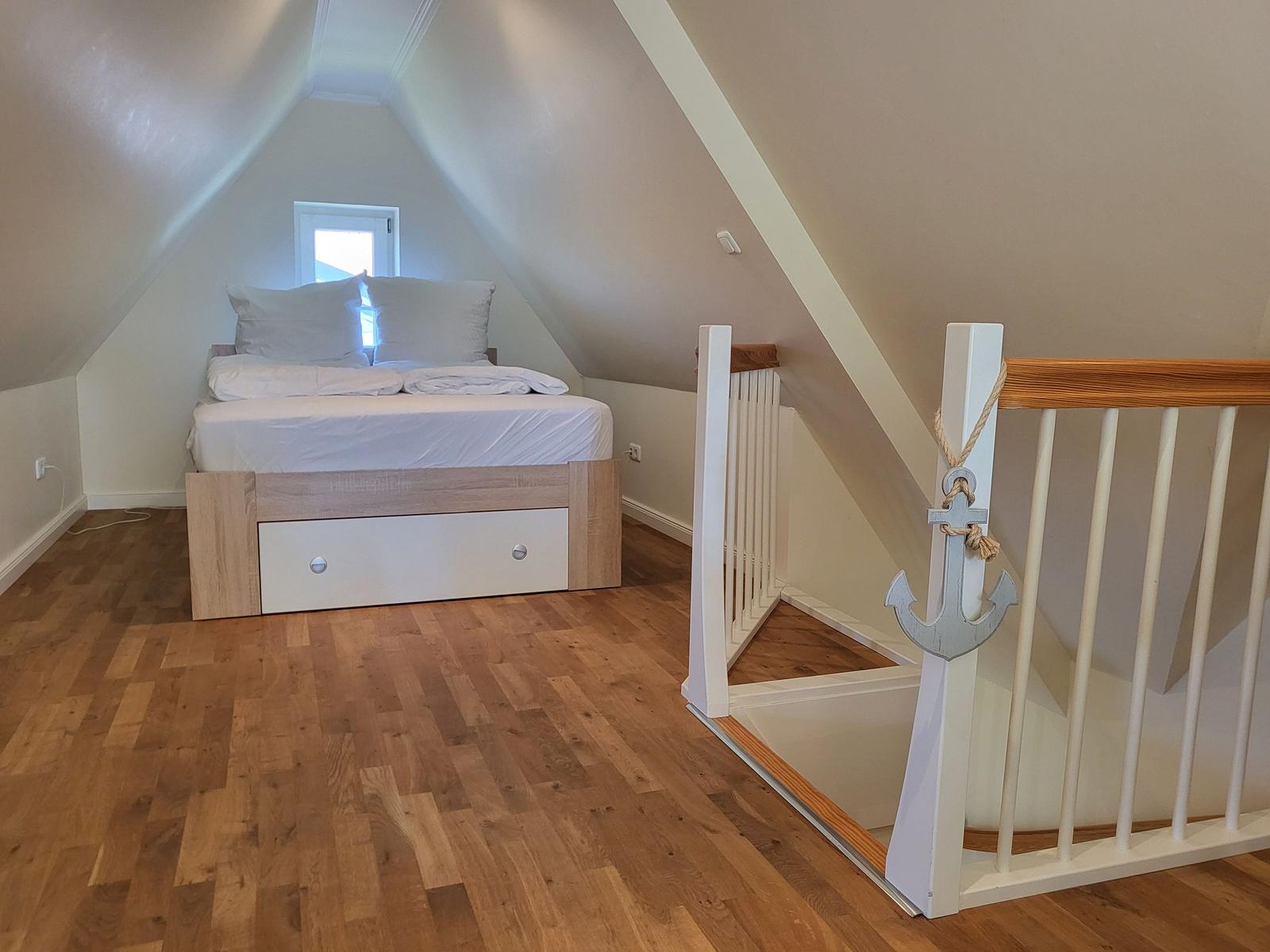 Schlafzimmer mit Dachschrägen, Bett und Holzboden. Geländer mit Ankerdekoration.