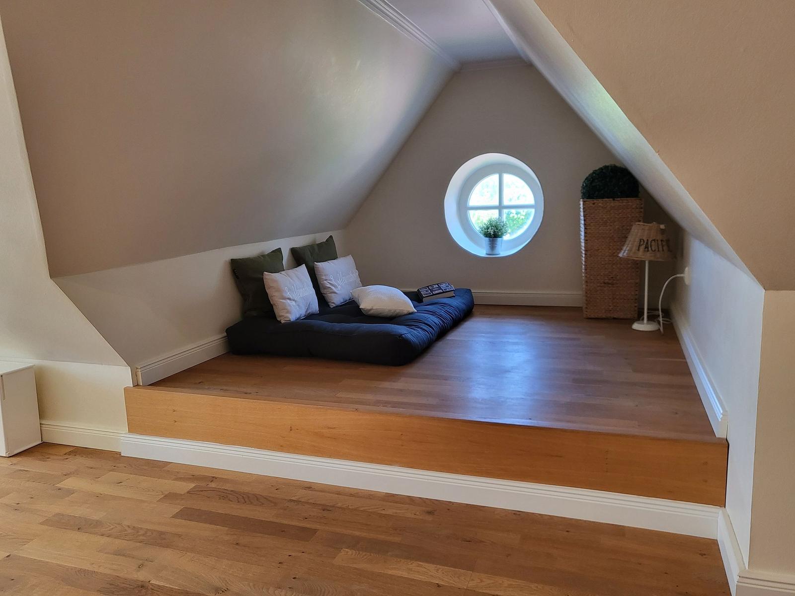 Dachgeschosszimmer mit Rundfenster, Matratze und Kissen auf Holzboden.