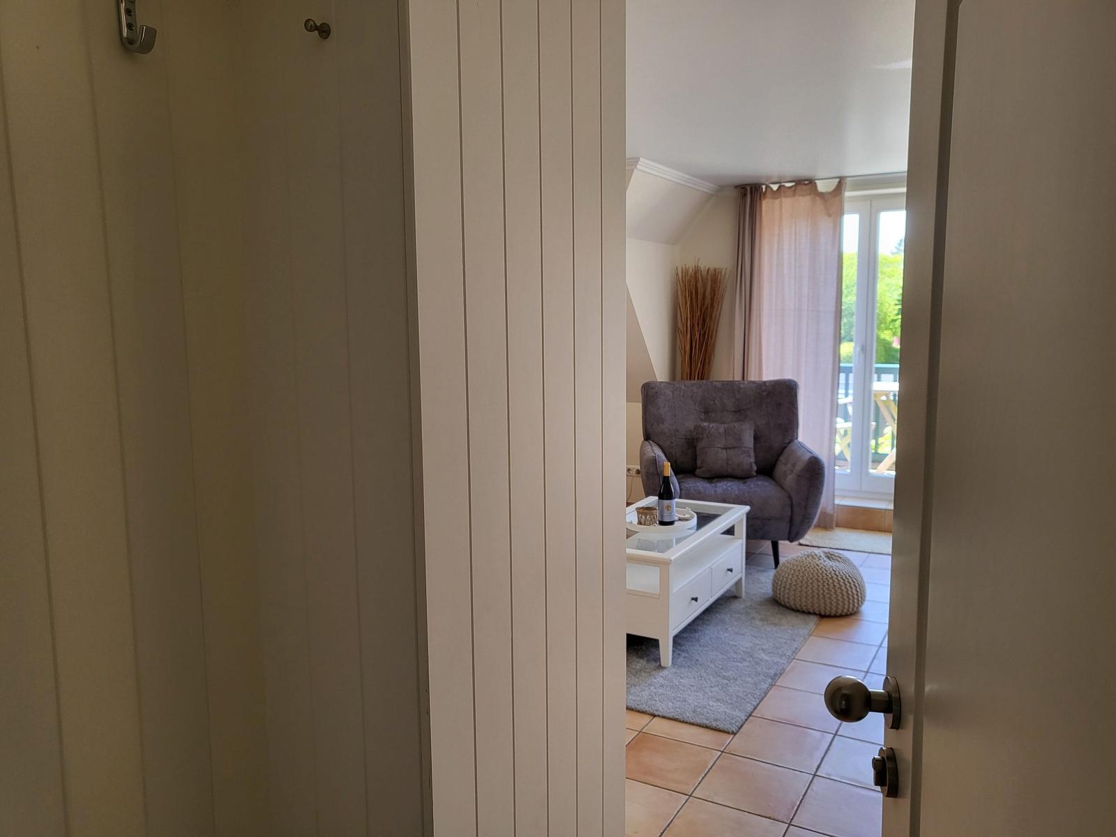 Durchgang in Wohnzimmer mit grauem Sessel und Tisch mit Weinflasche.