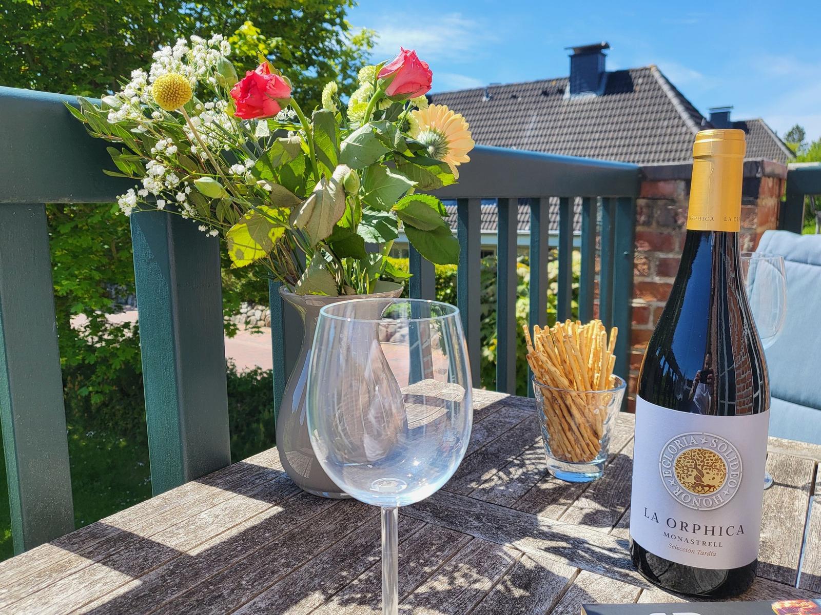 Auf der Terrasse steht ein Tisch mit Wein, Cracker und Blumen.